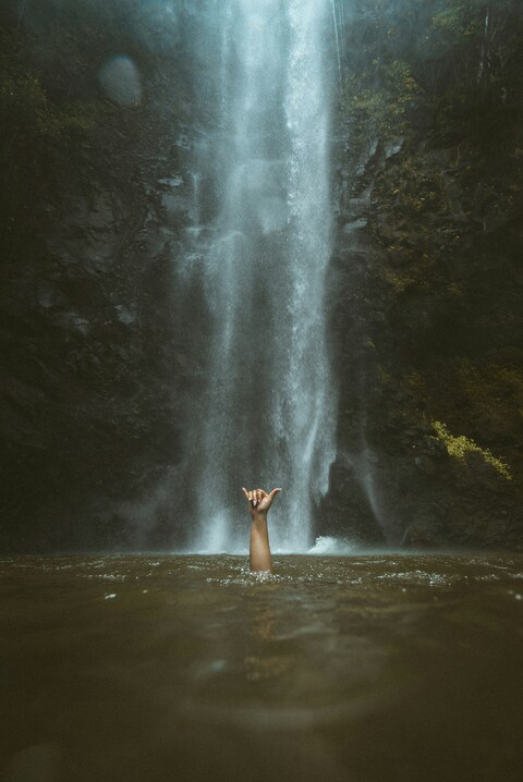 Raised Hand Under Tall Waterfall