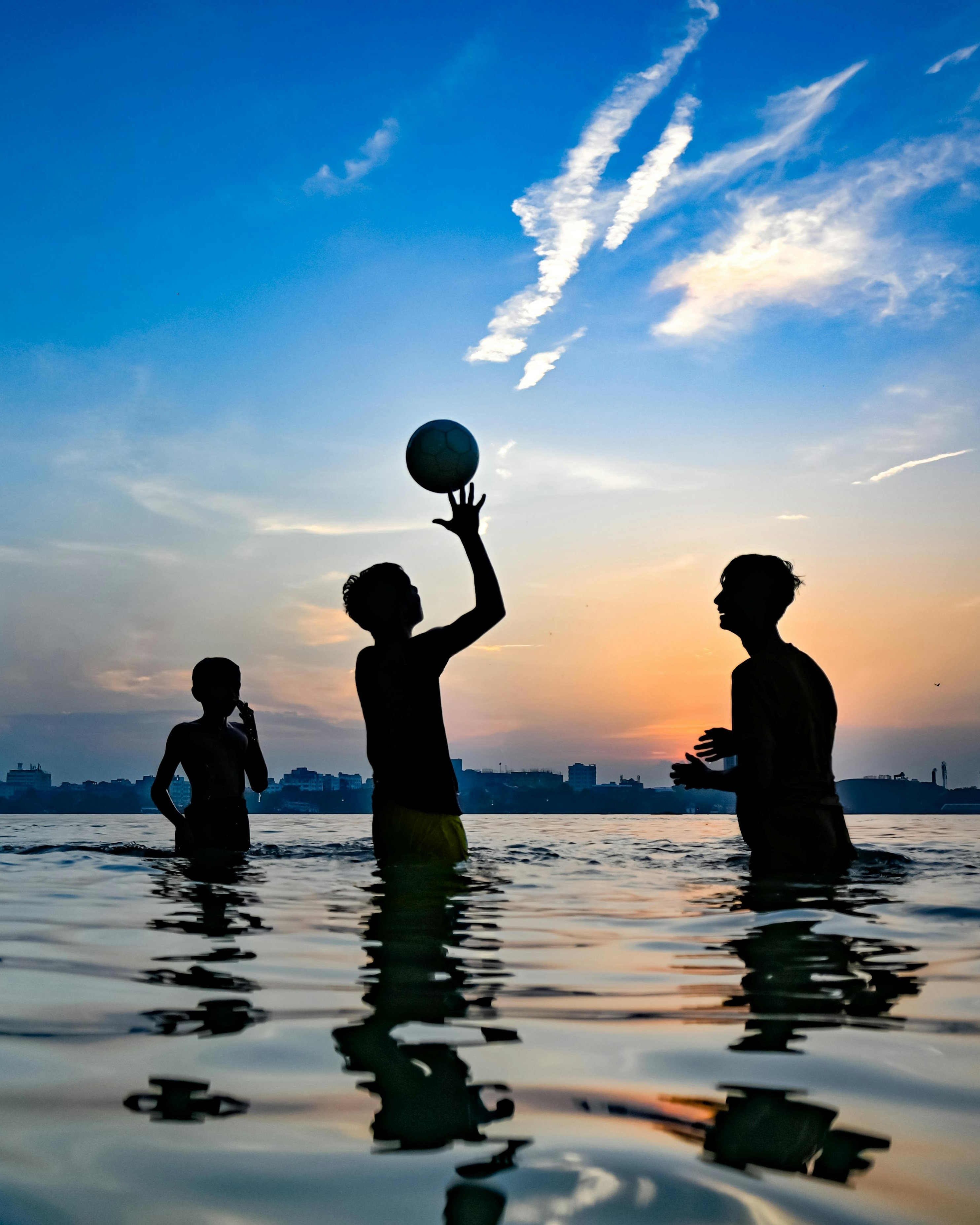 Three Boys Playing Ball In River At Sunset