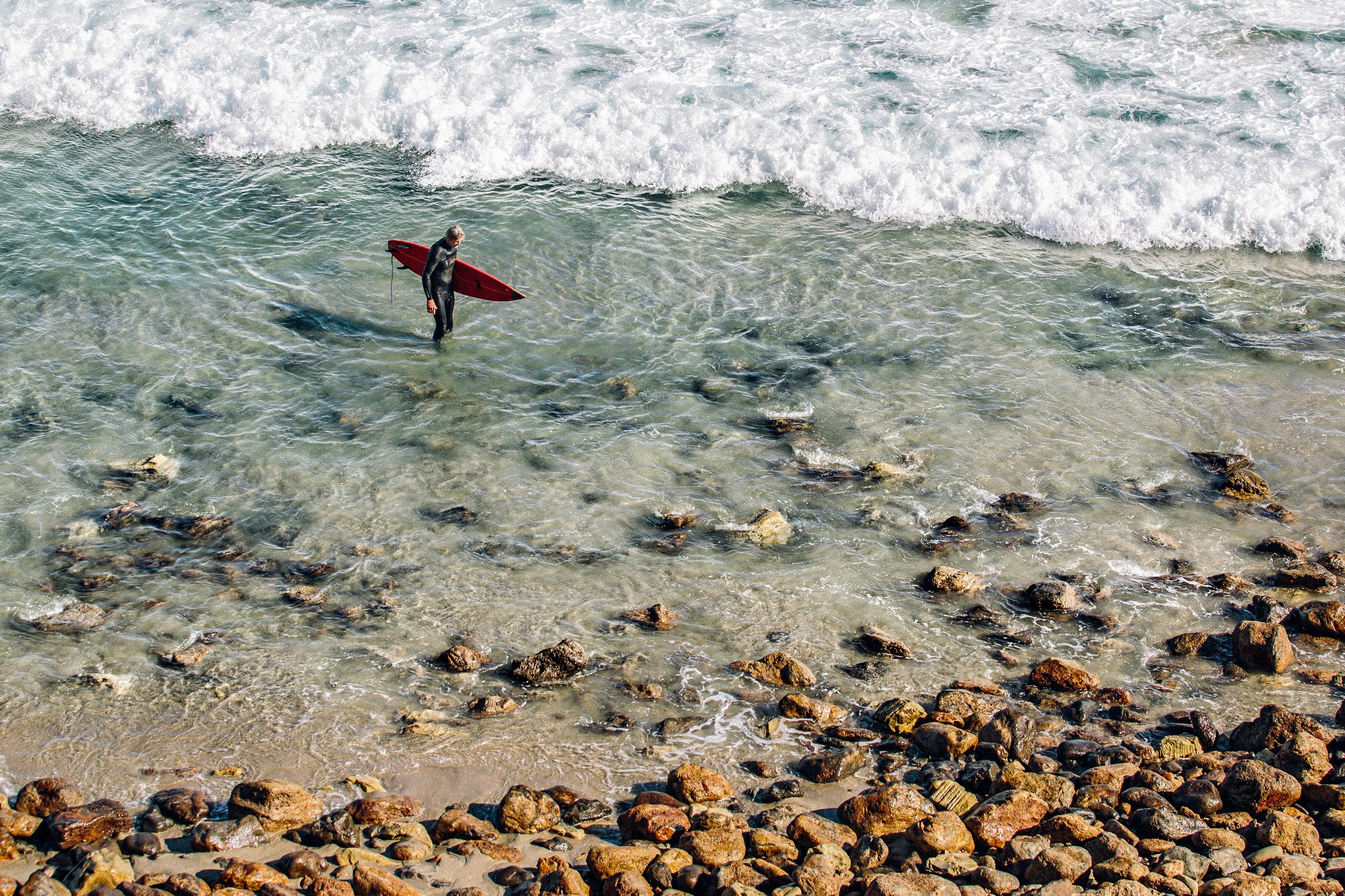 Surfer with Red Surfboard in Shallow Rocky Sea