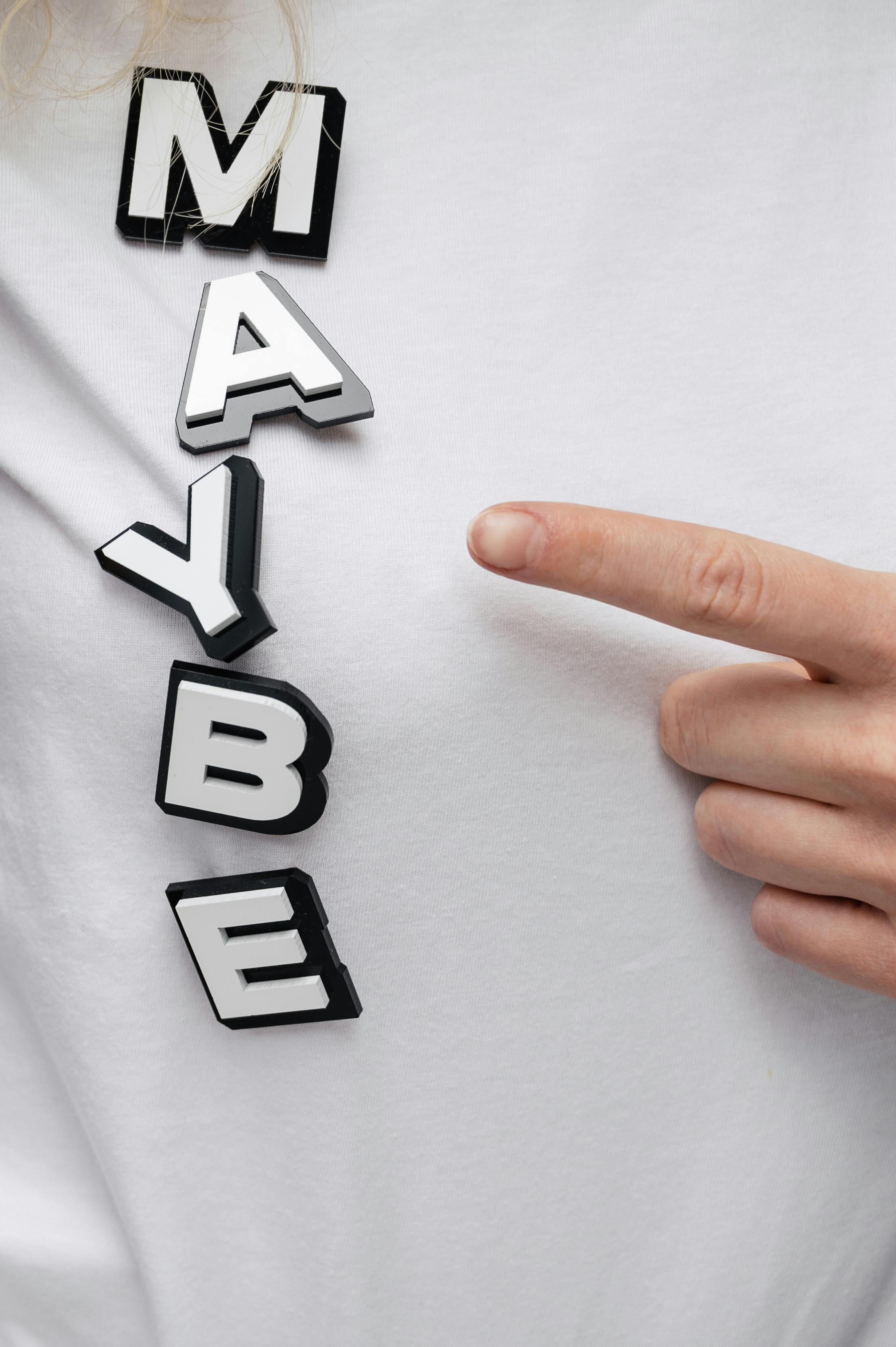 Hand Pointing To MAYBE Text On Shirt
