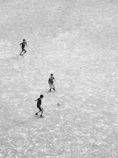 Three Boys Playing Soccer on Dirt Ground