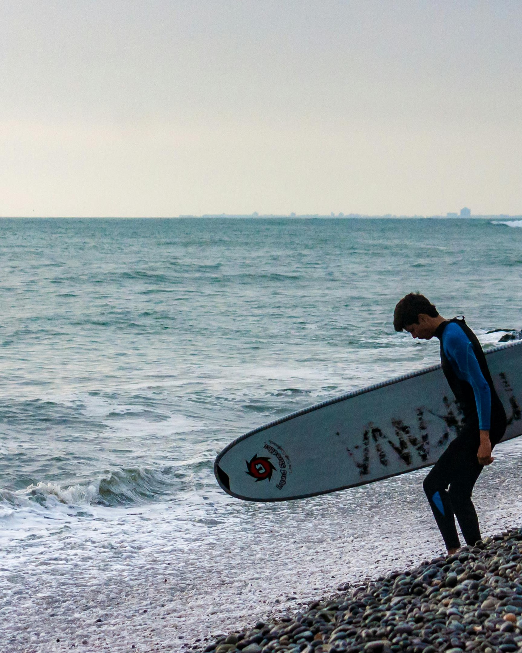 Surfer Carrying Board on Pebble Beach