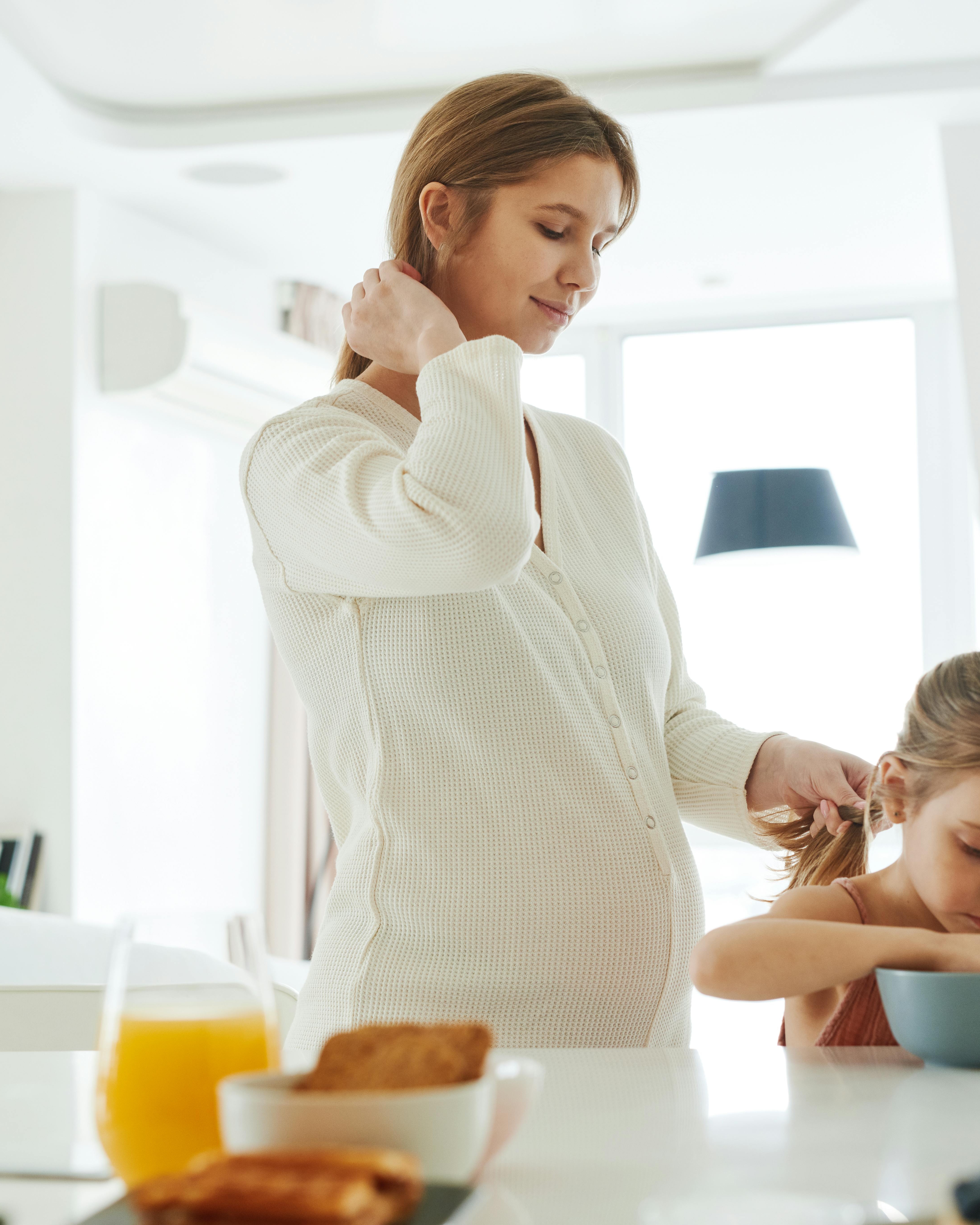 Pregnant Mom Fixing Daughter's Hair at Breakfast