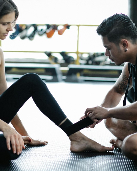 Trainer Taping Client's Ankle In Gym