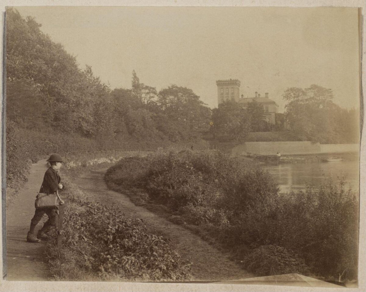 Boy Walking by River Toward Tower House