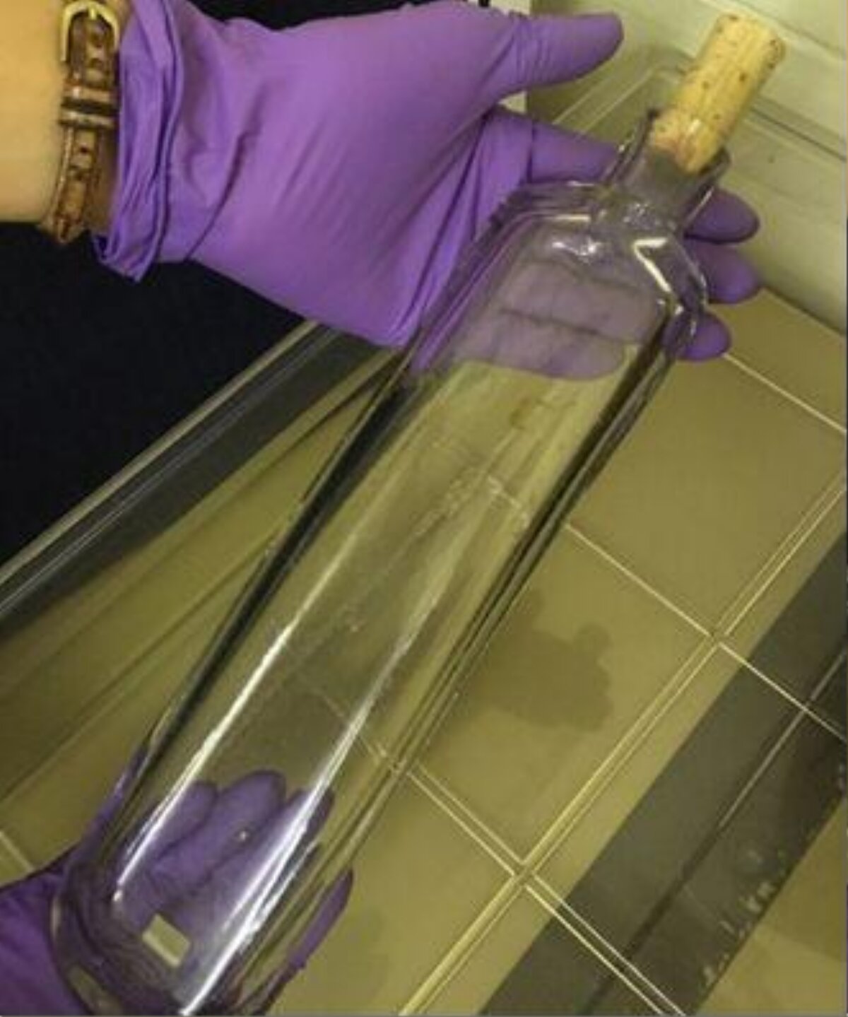 Long Glass Bottle Held by Purple Gloved Hands