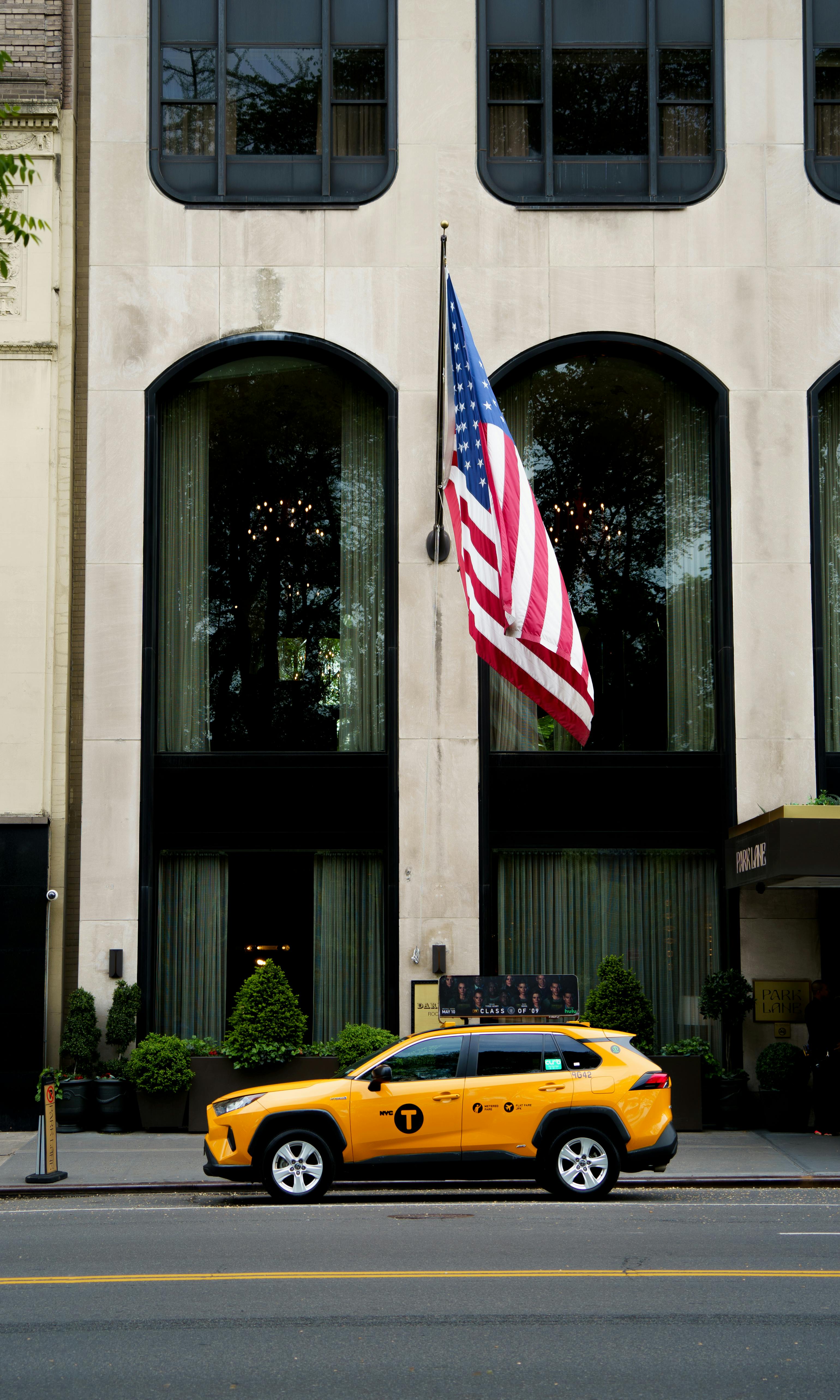 Yellow NYC Taxi by Building with US Flag
