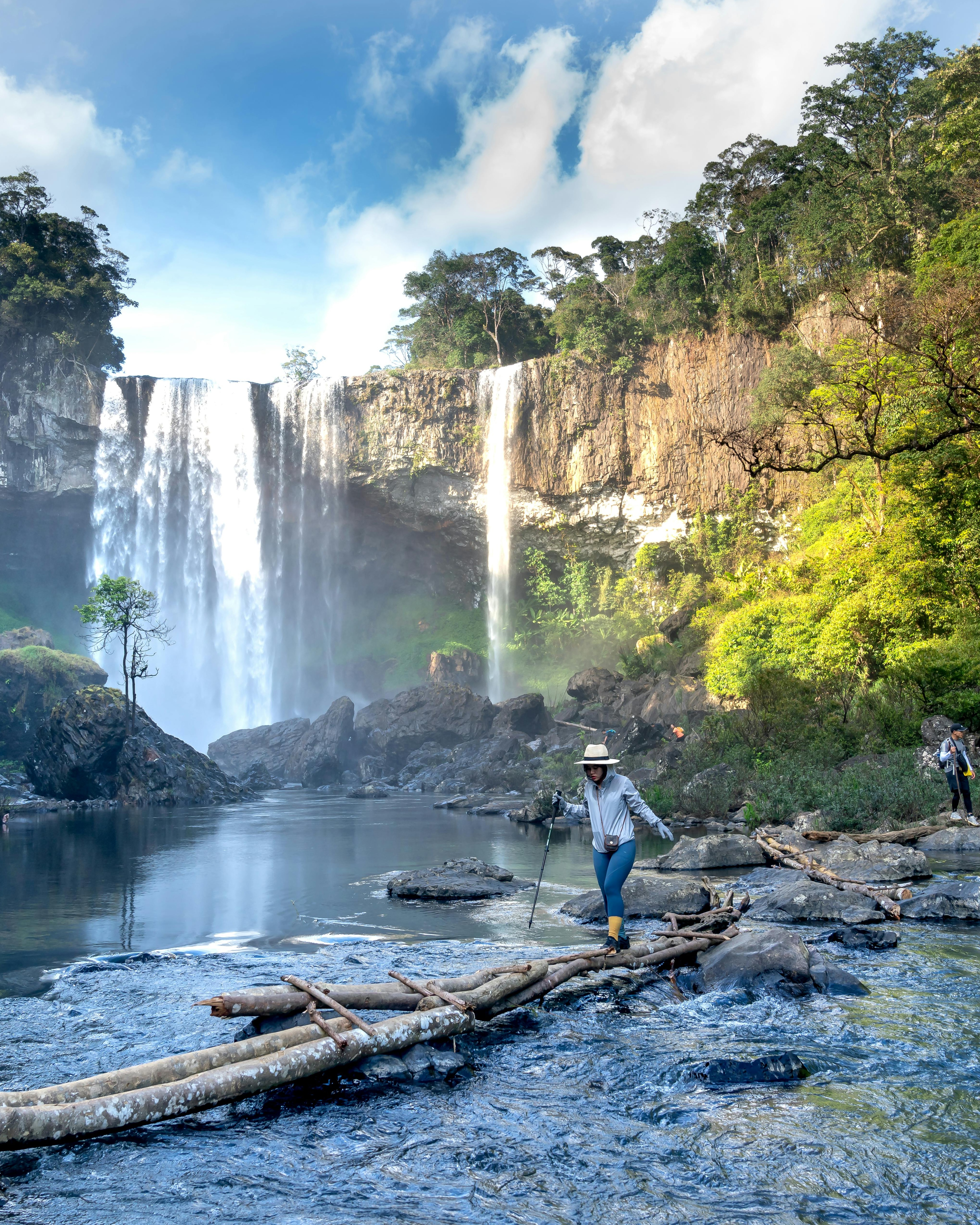 Hiker Crossing River by Waterfall
