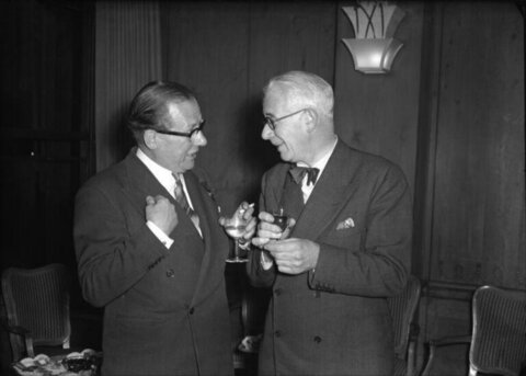 Two Gentlemen Conversing Over Drinks