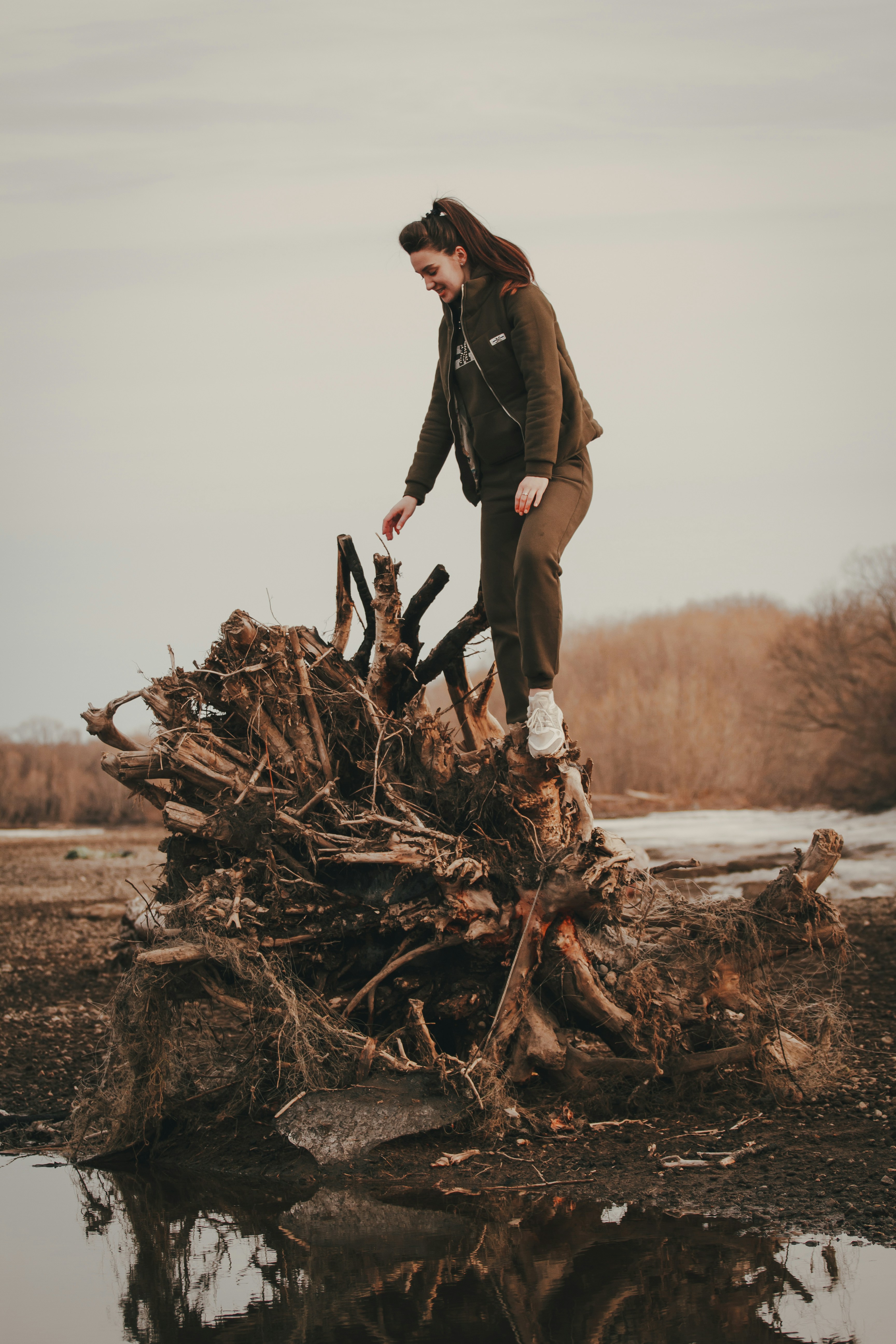 Woman Standing on Uprooted Tree by Water