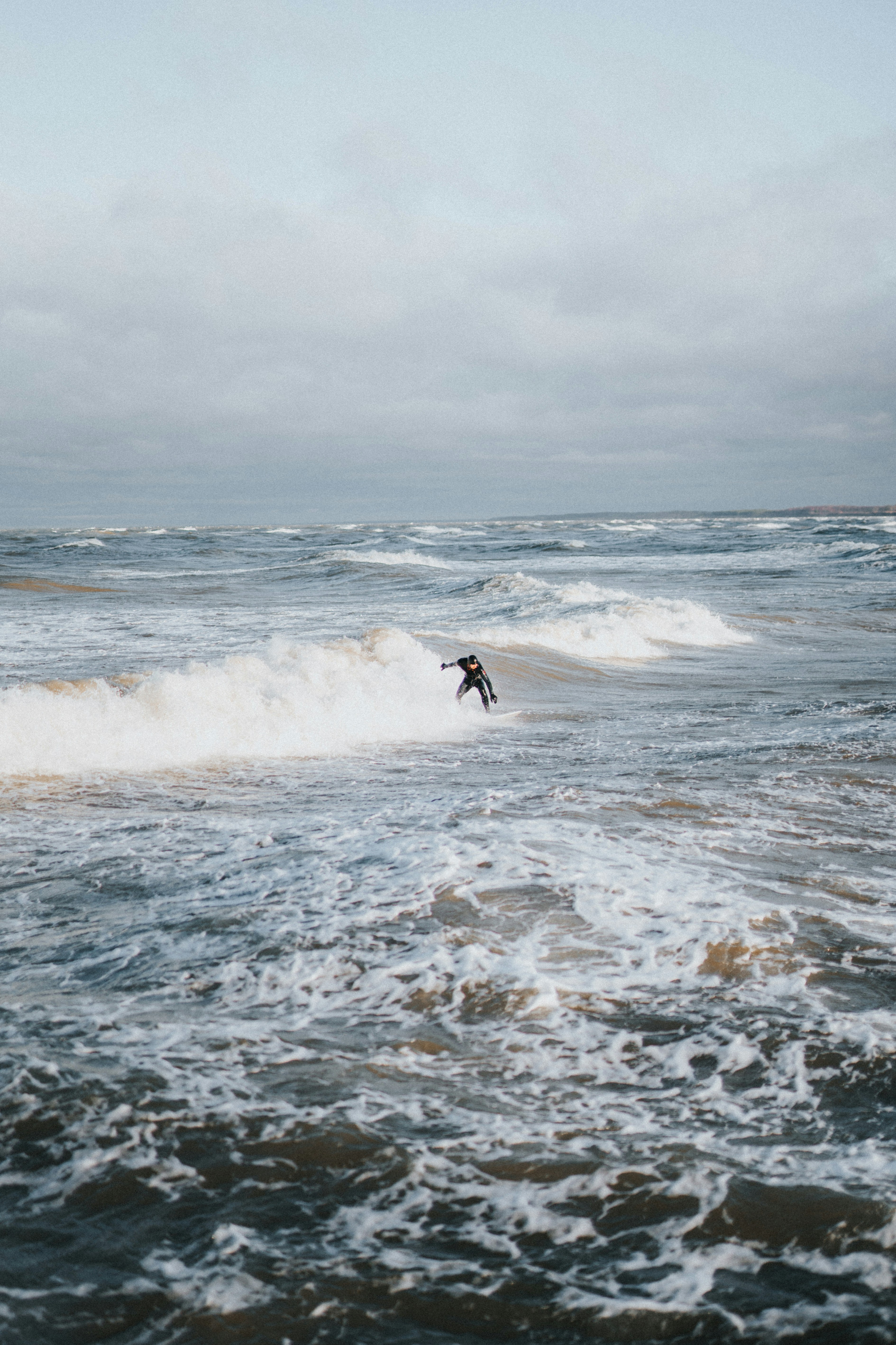 Surfer Riding Wave on Overcast Sea