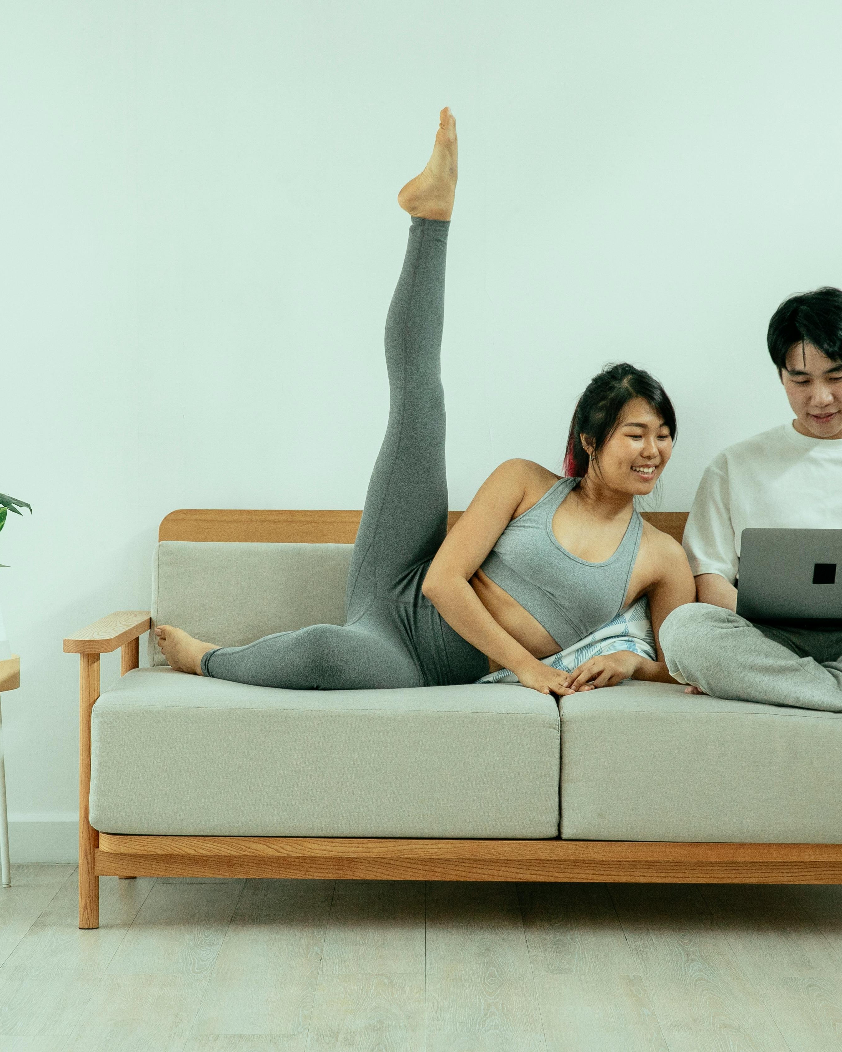 Woman Stretching on Sofa Beside Man With Laptop