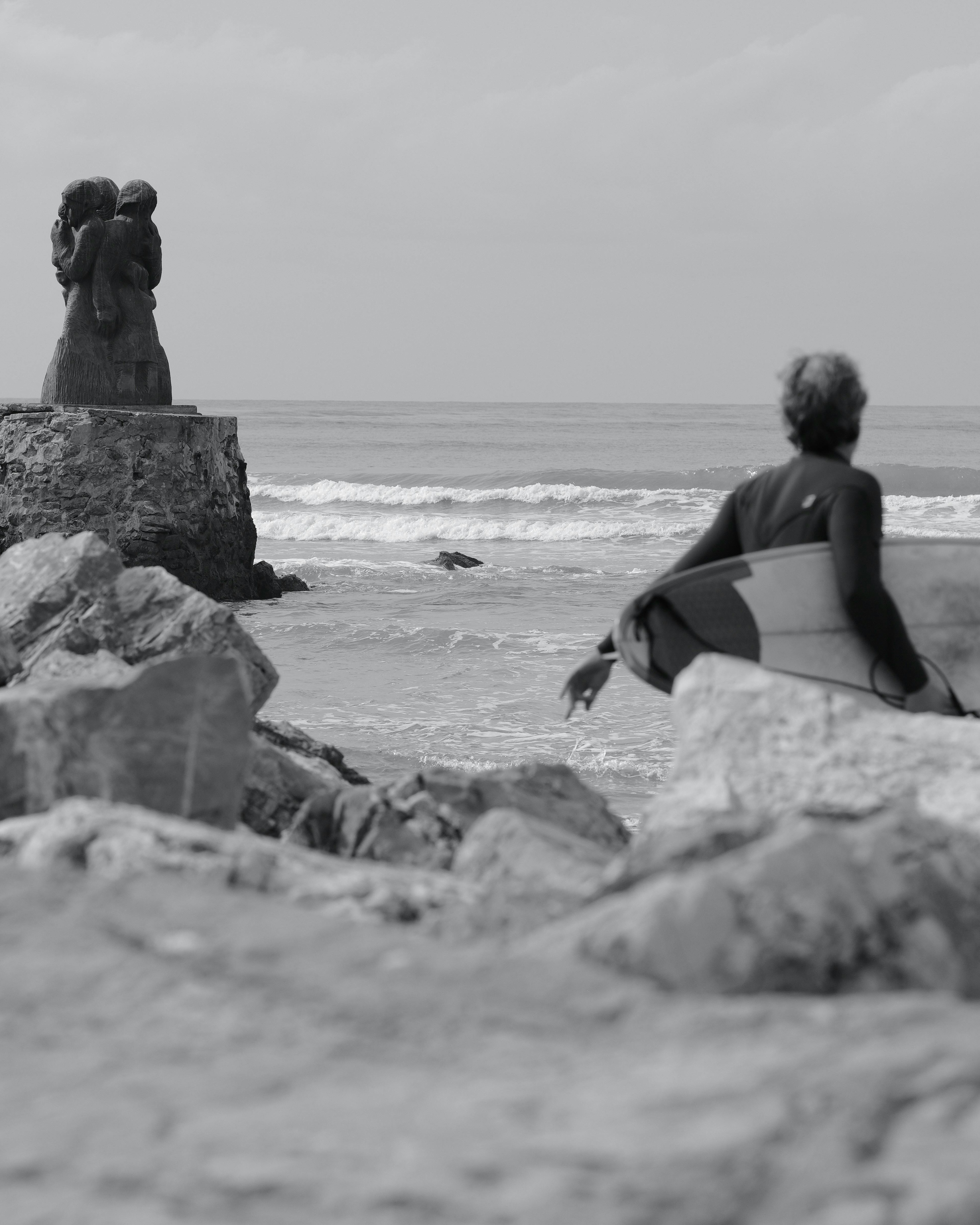 Surfer Heading to Sea by Coastal Statue