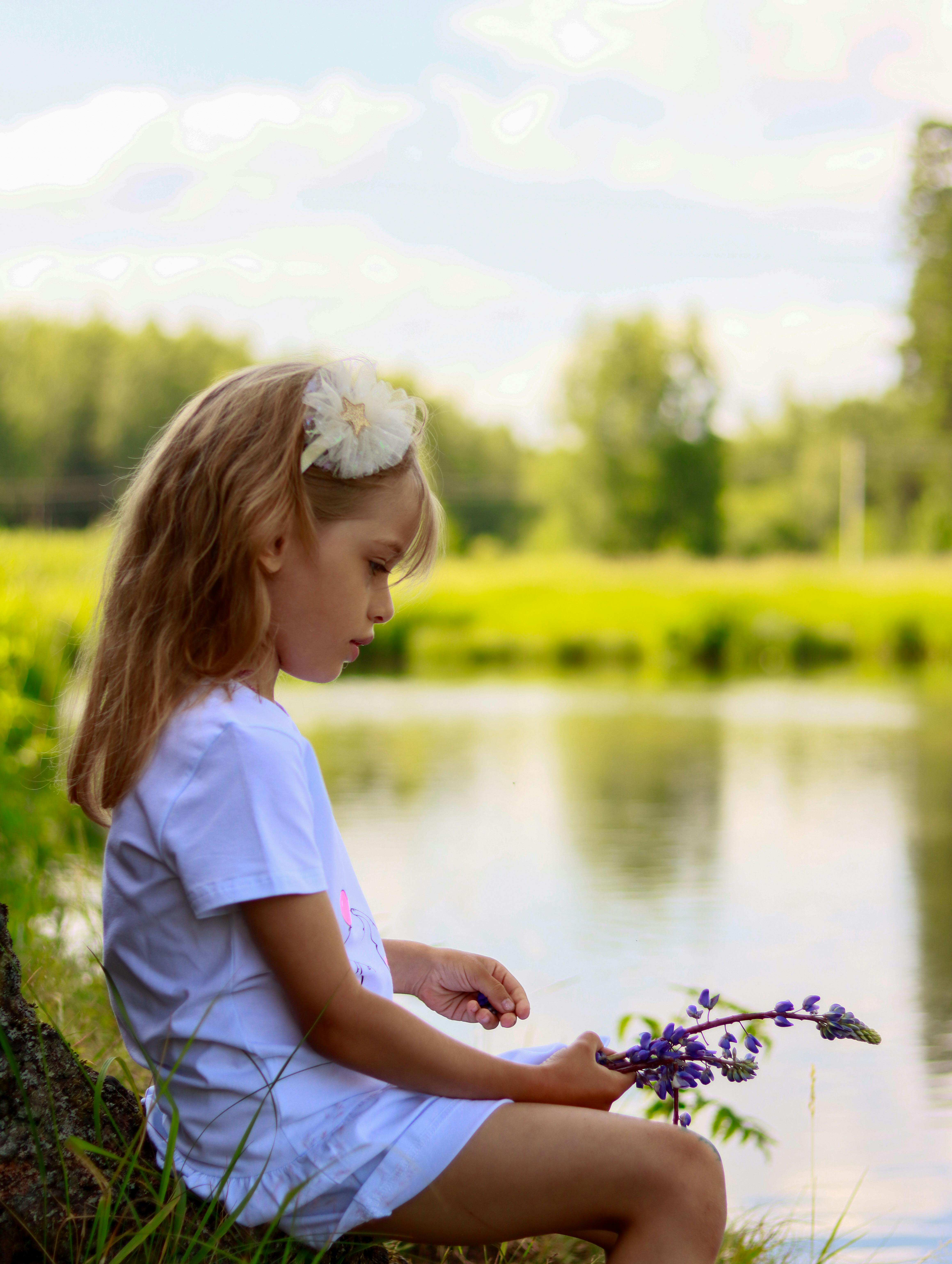 Little Girl By Lakeside Holding Purple Flowers