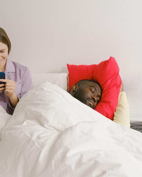 Man Sleeping While Woman Uses Phone in Bed