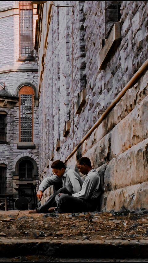 Two Inmates Resting Against Prison Wall