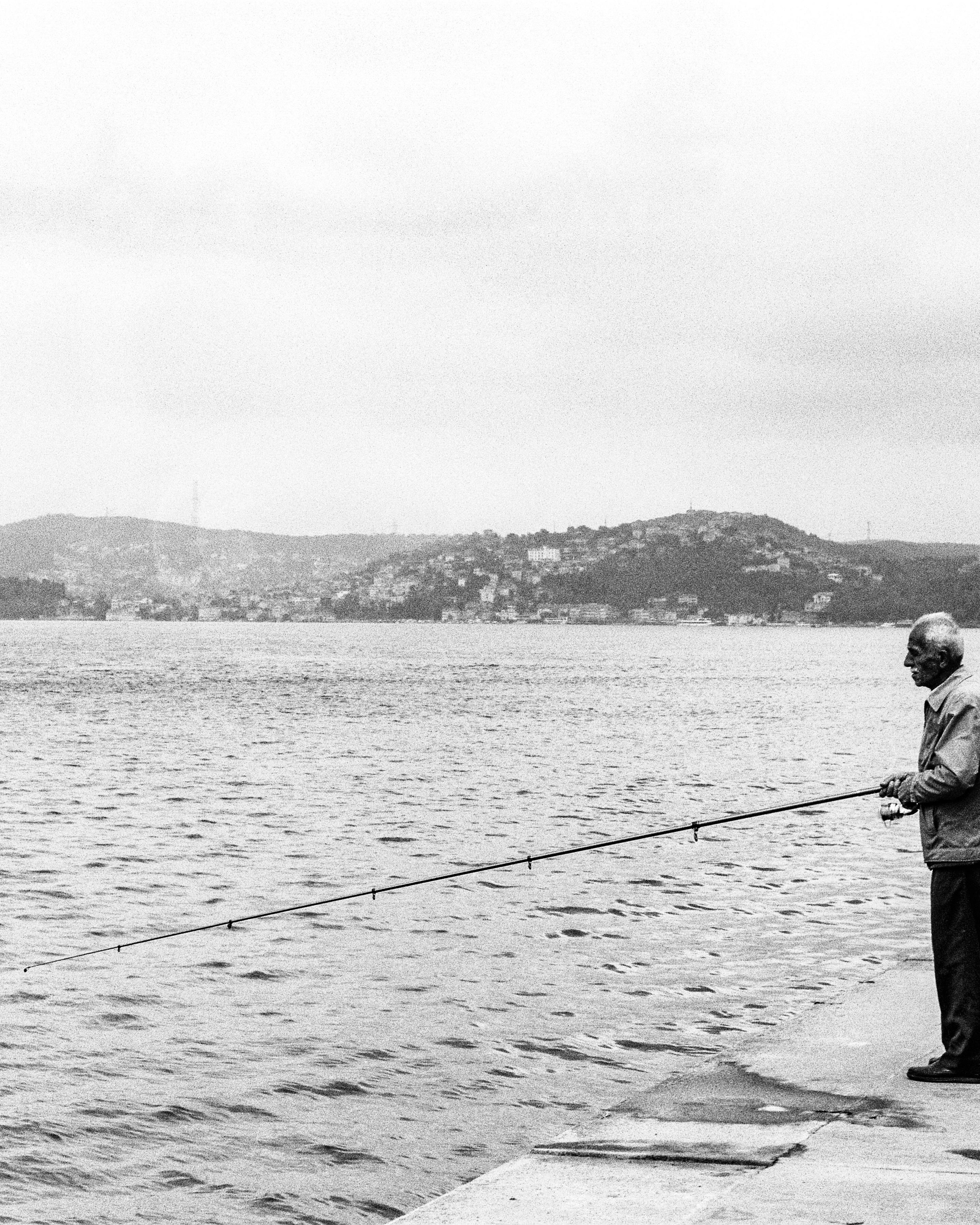 Elderly Man Fishing By Waterfront