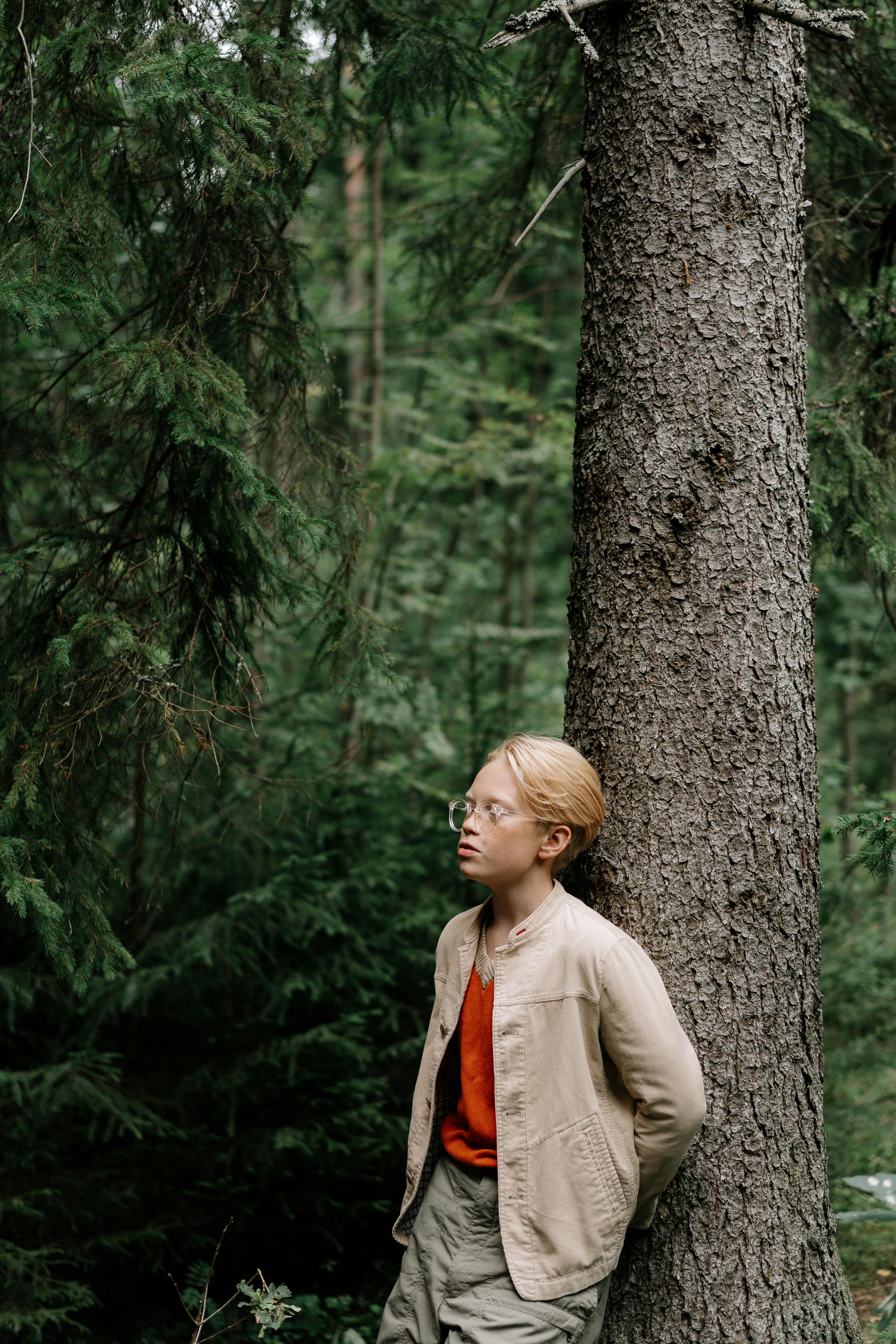 Blonde Boy Leaning on Tree in Forest
