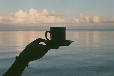 Hand Holding Coffee Over Calm Sea