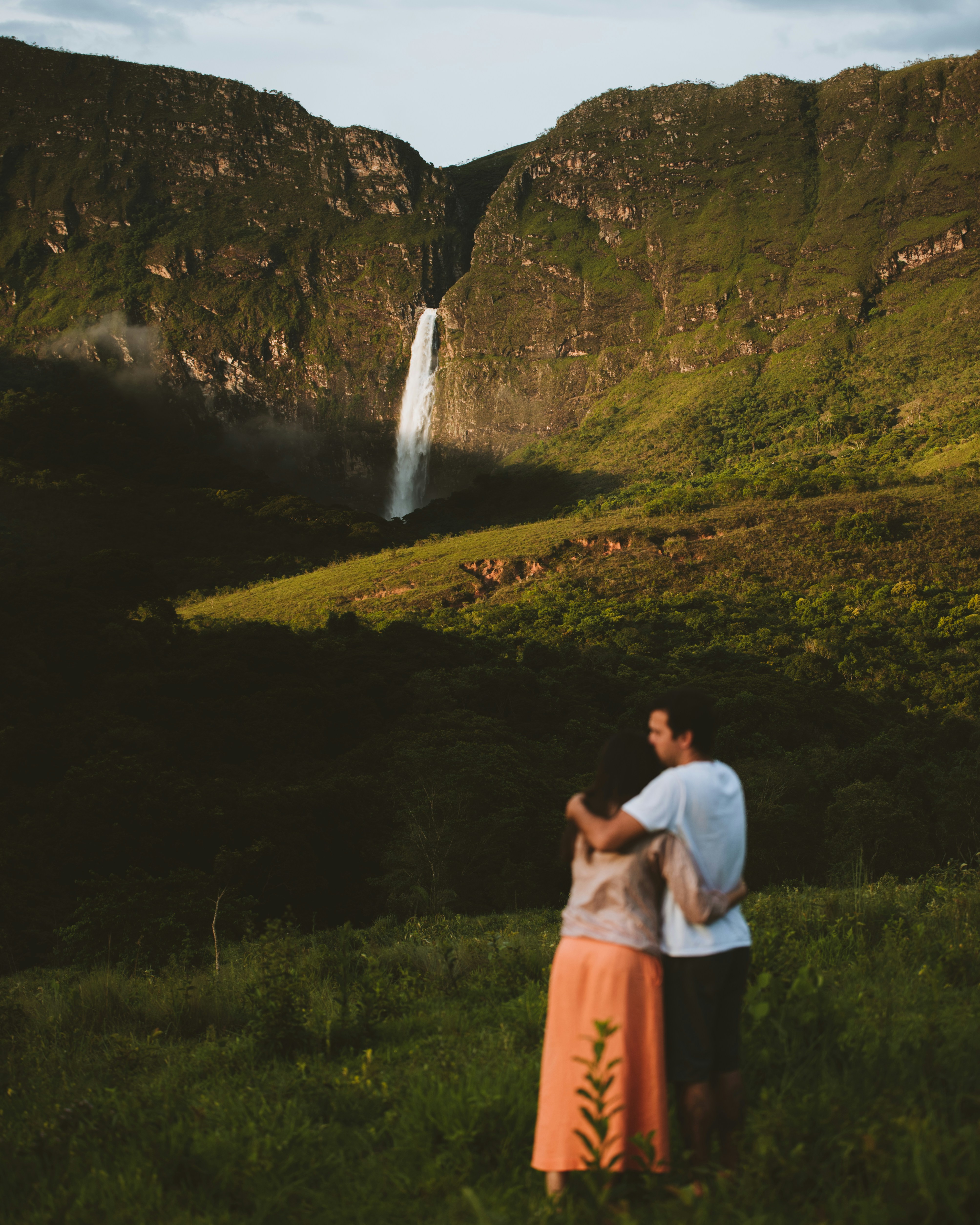 Couple Embracing Before Mountain Waterfall