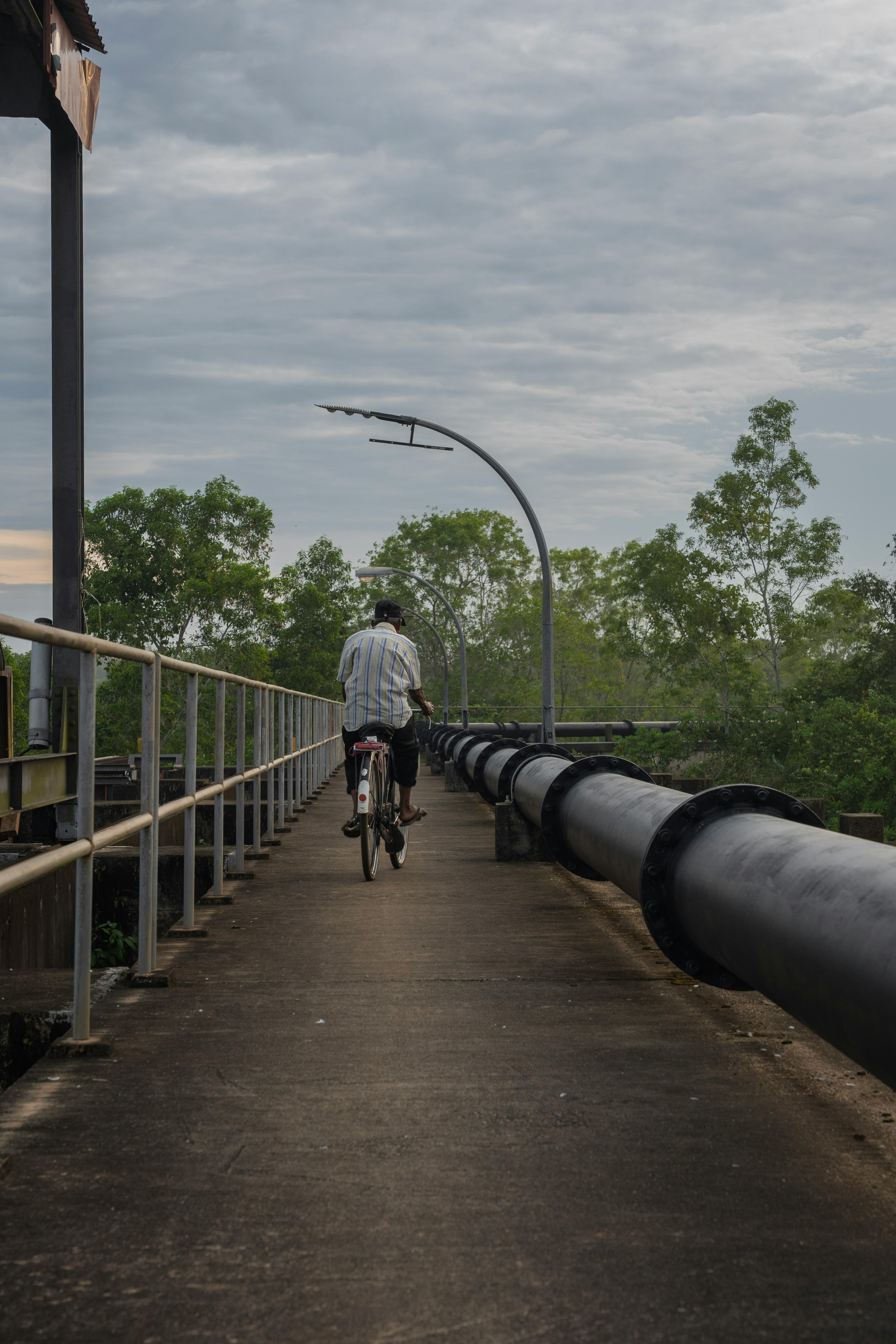 Person Cycling on Bridge Walkway