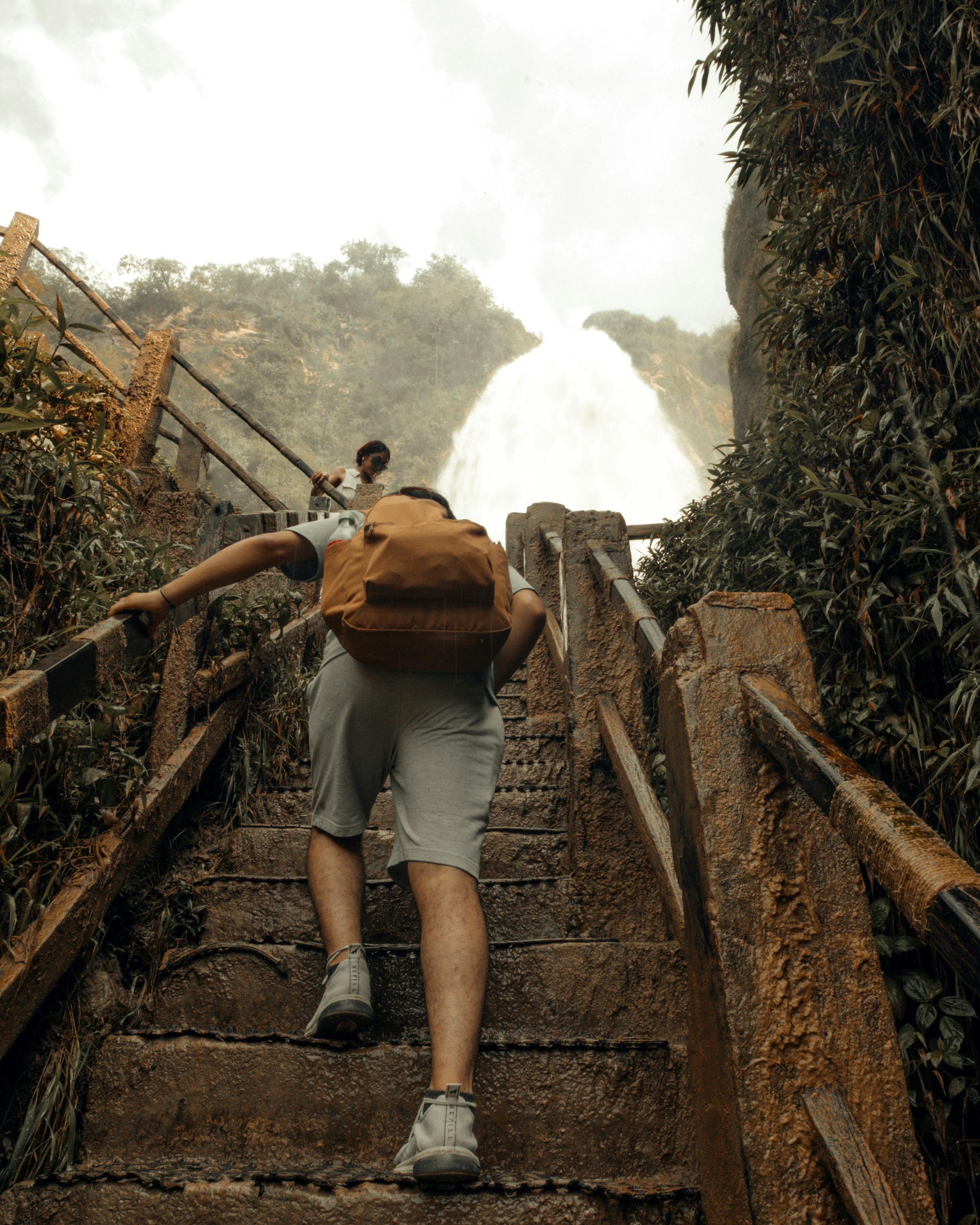 Hiker Climbing Stairs Toward Waterfall