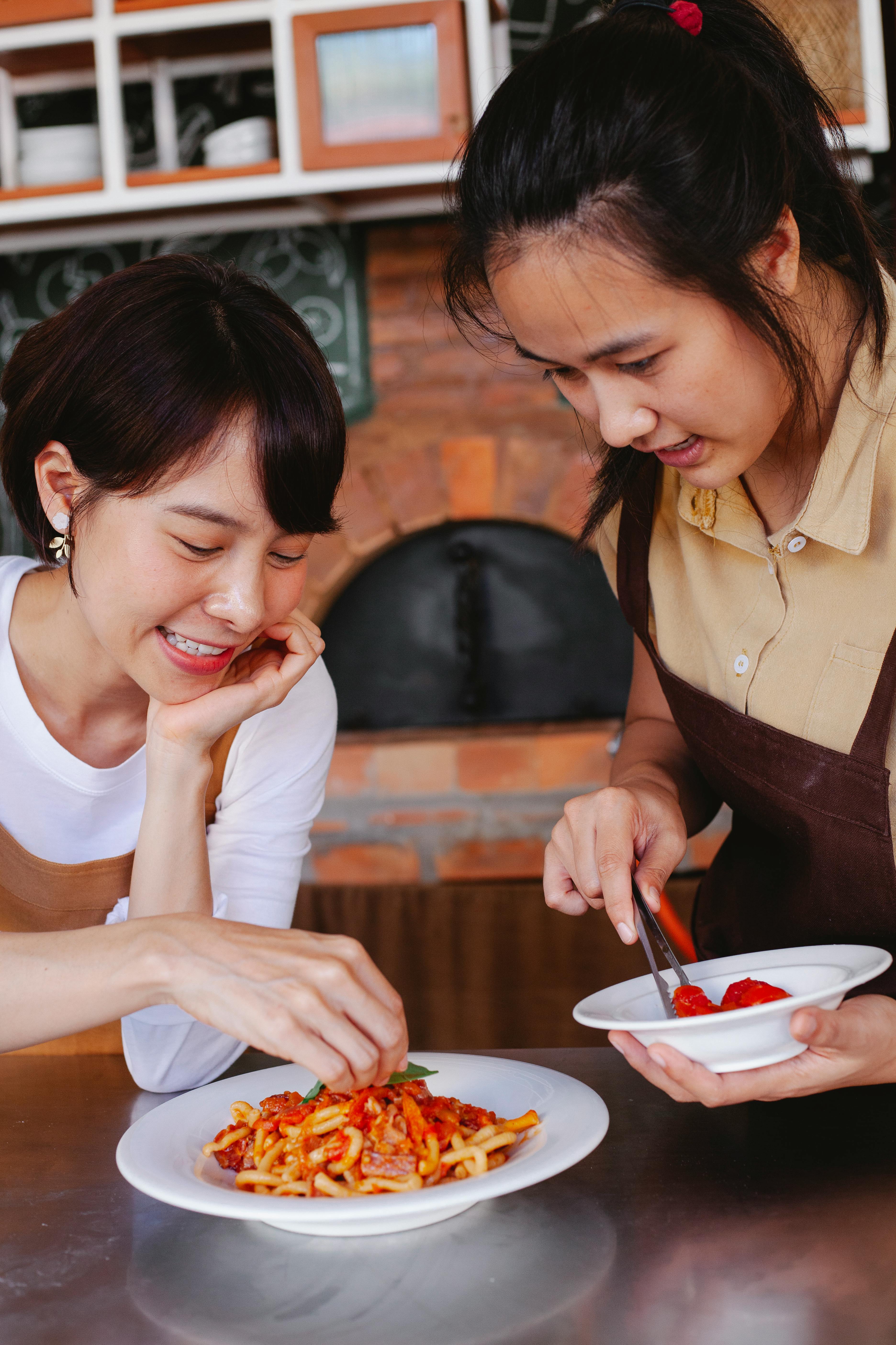 Two Women Garnishing Pasta Dish