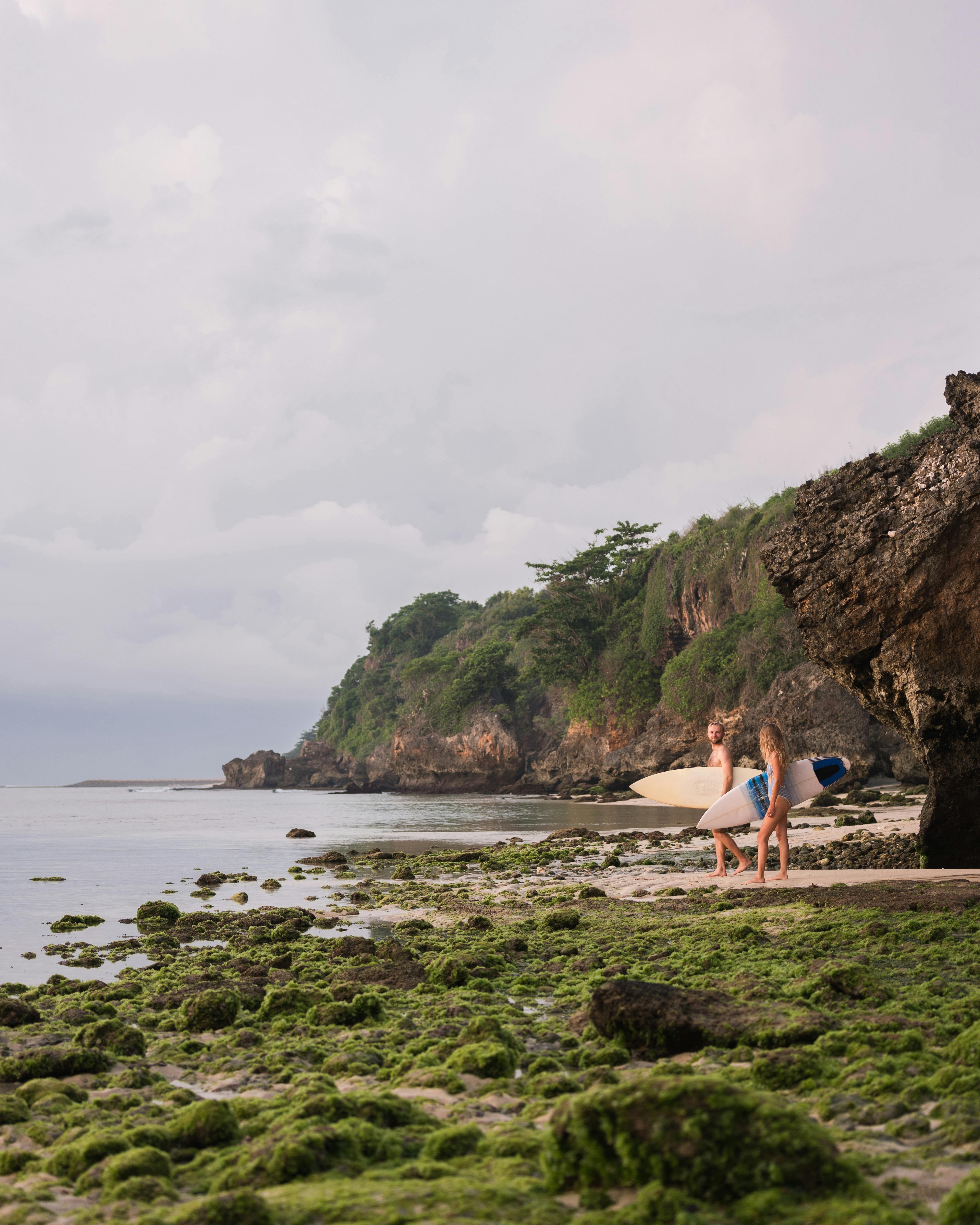 Two Surfers Walking Along Mossy Rocky Coast