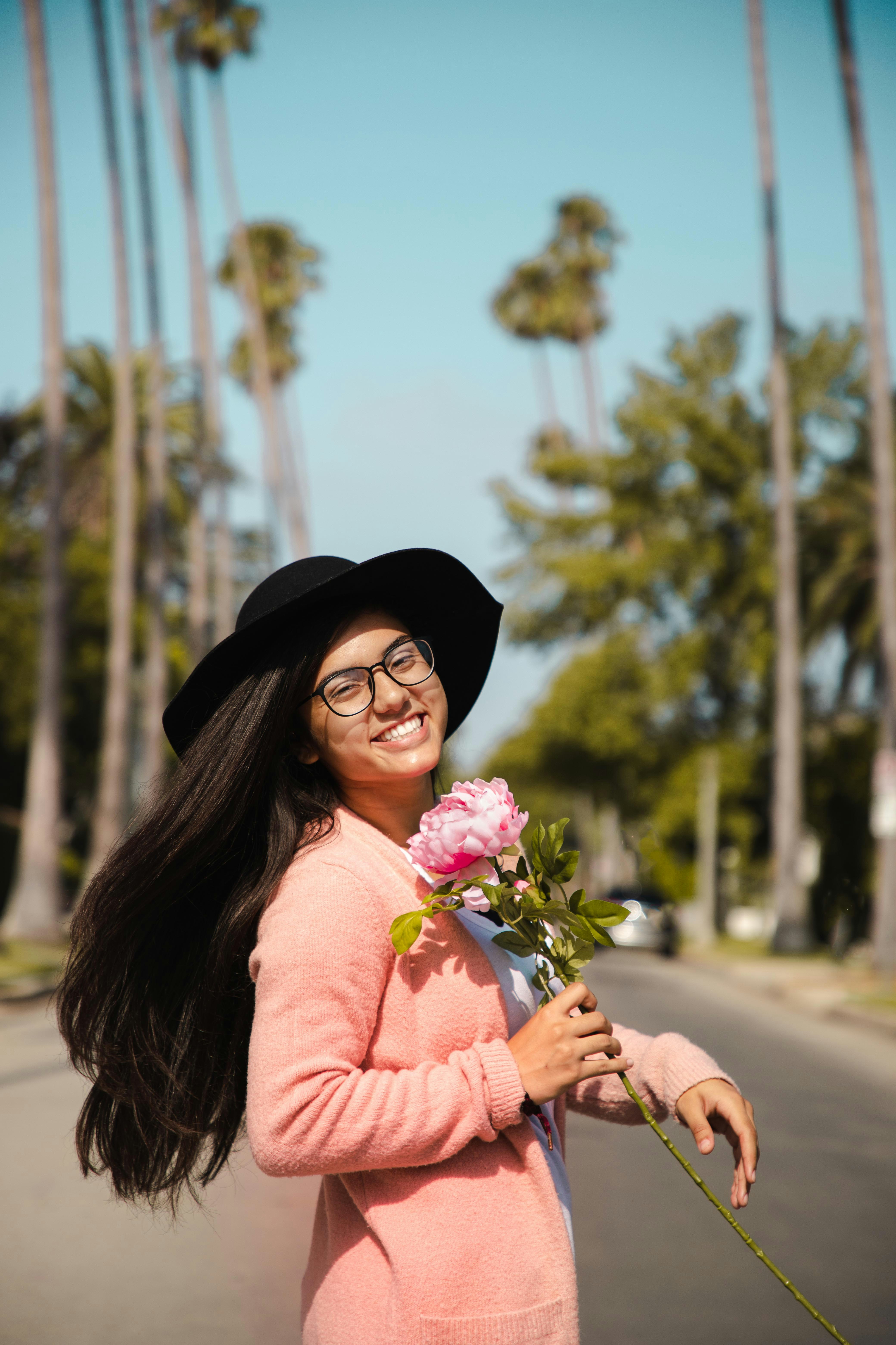 Smiling Girl Holding Flower on Palm-Lined Street