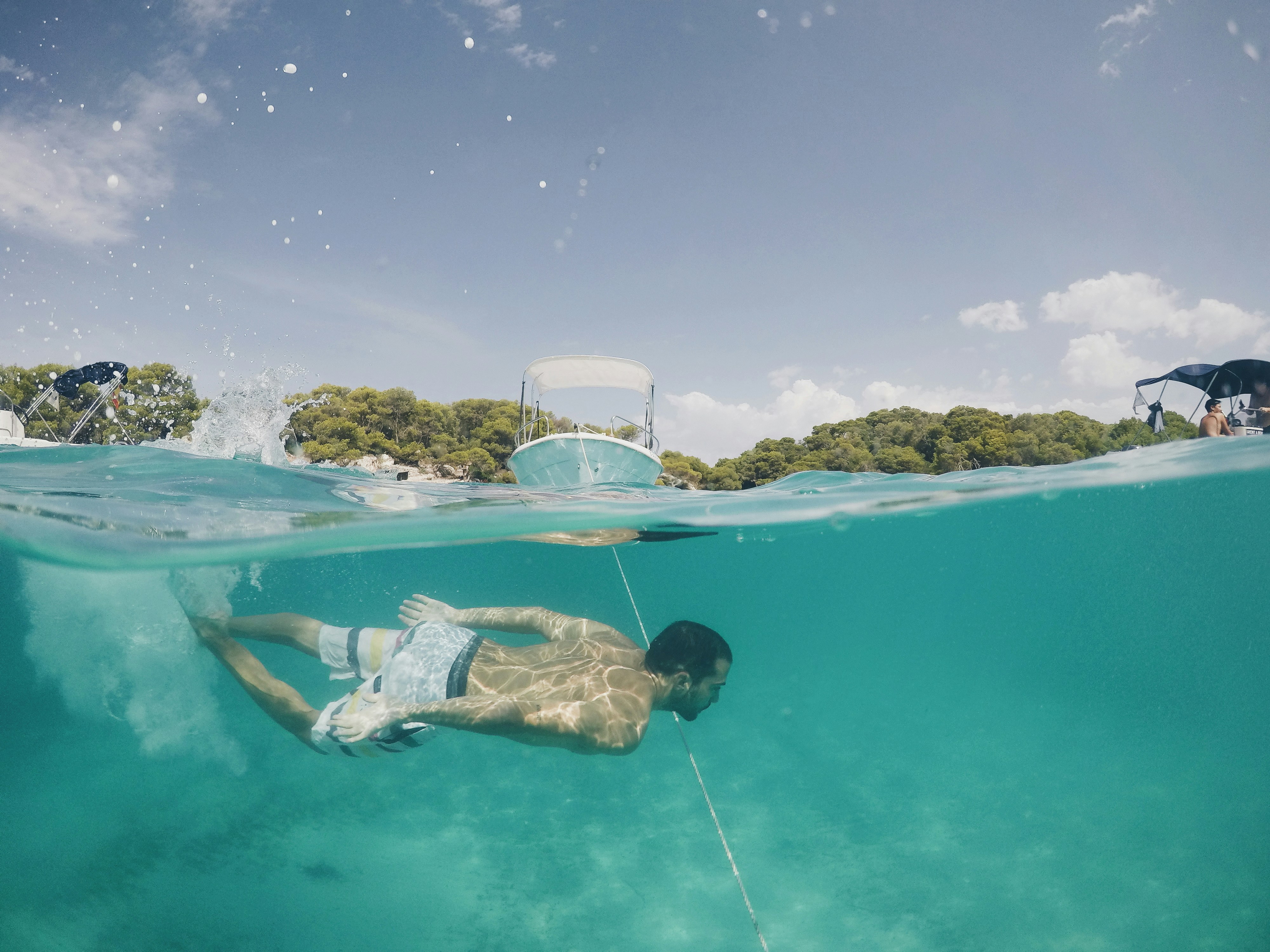 Man Swimming Underwater Near Anchored Boats
