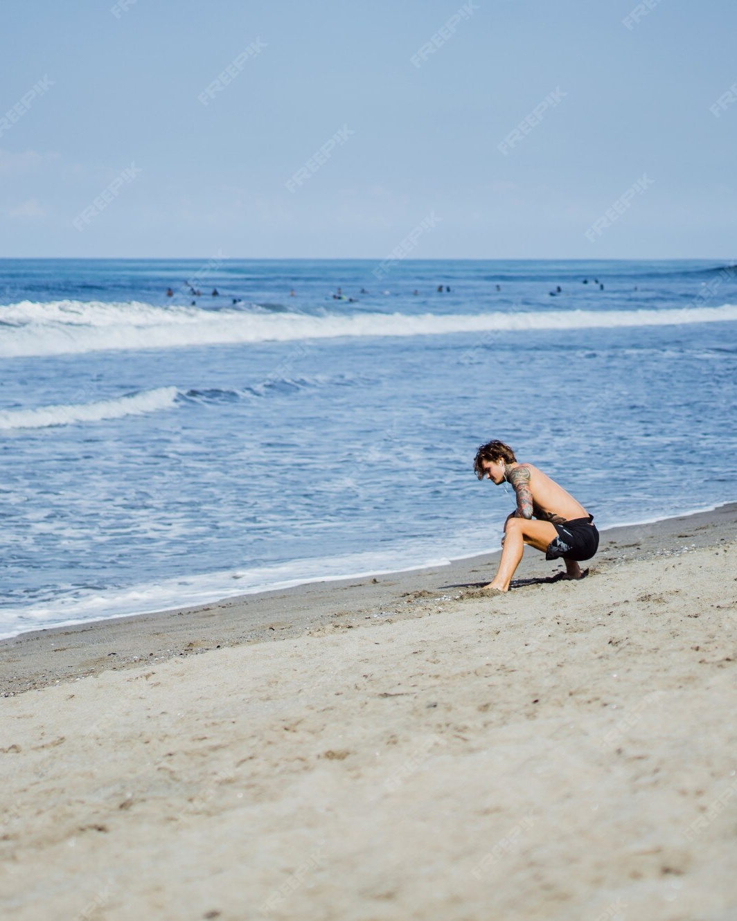 Tattooed Man Crouching on Beach Shore