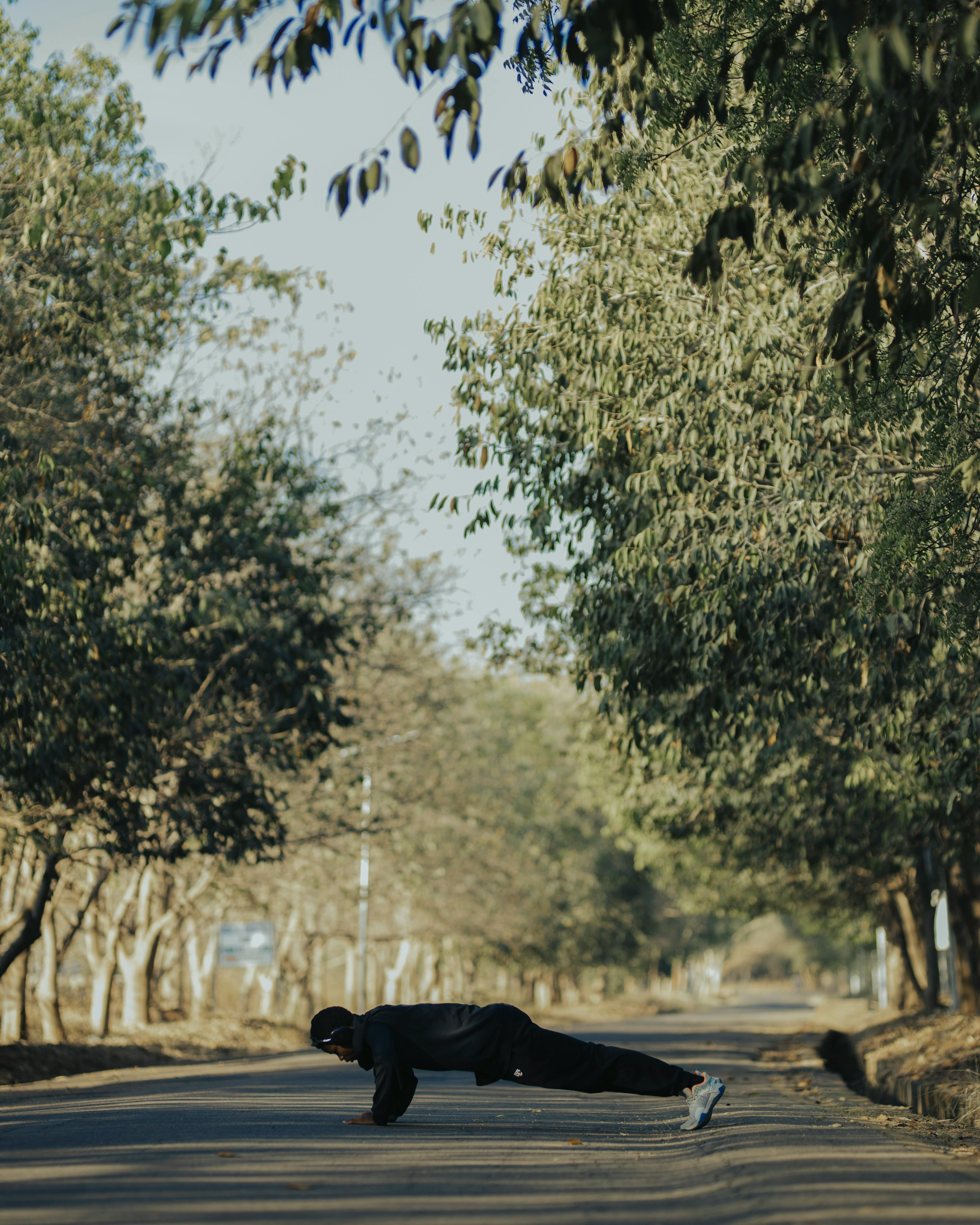 Man Doing Pushups on Tree-Lined Road