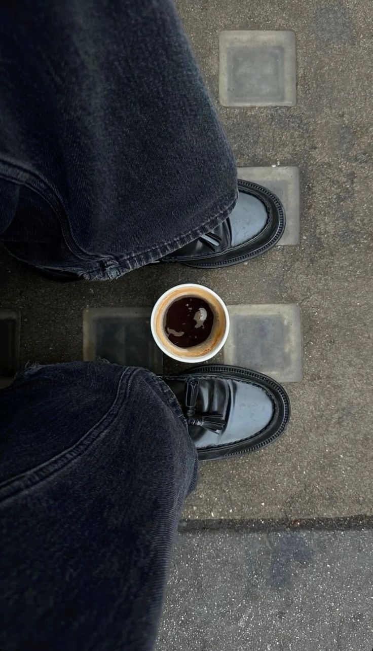 Coffee Between Standing Feet on Pavement