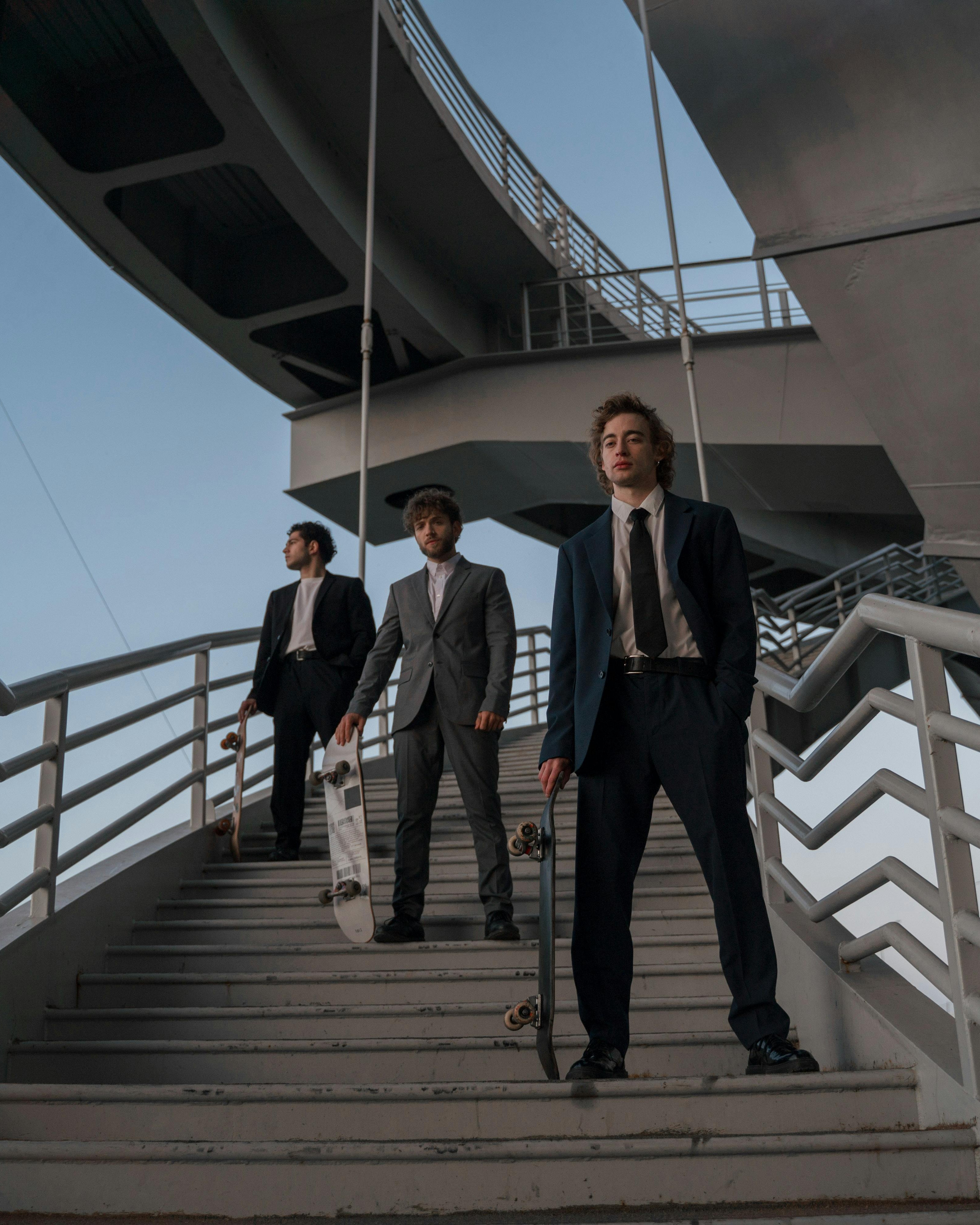 Three Men In Suits With Skateboards On Stairs
