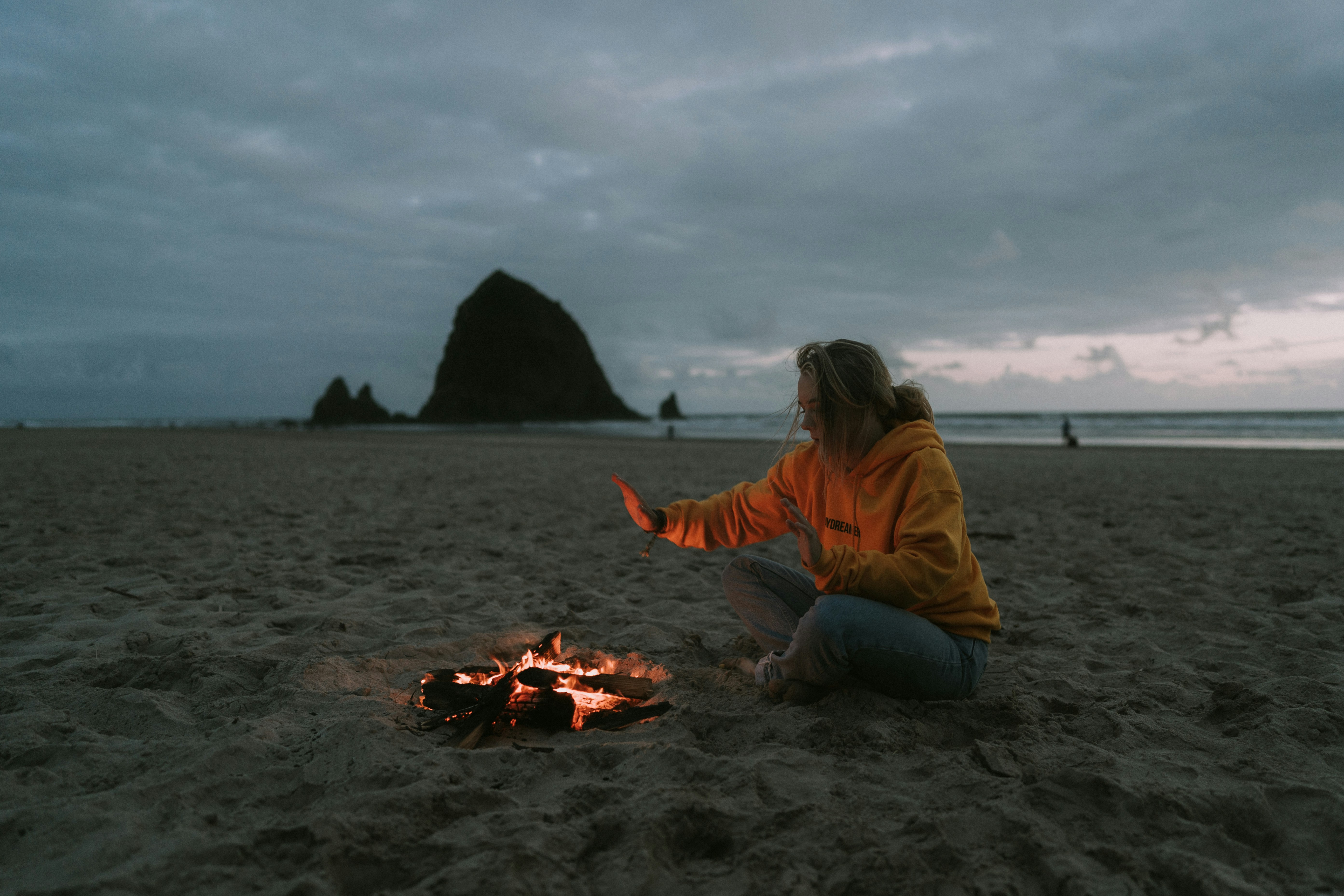 Girl Warming by Beach Campfire at Dusk