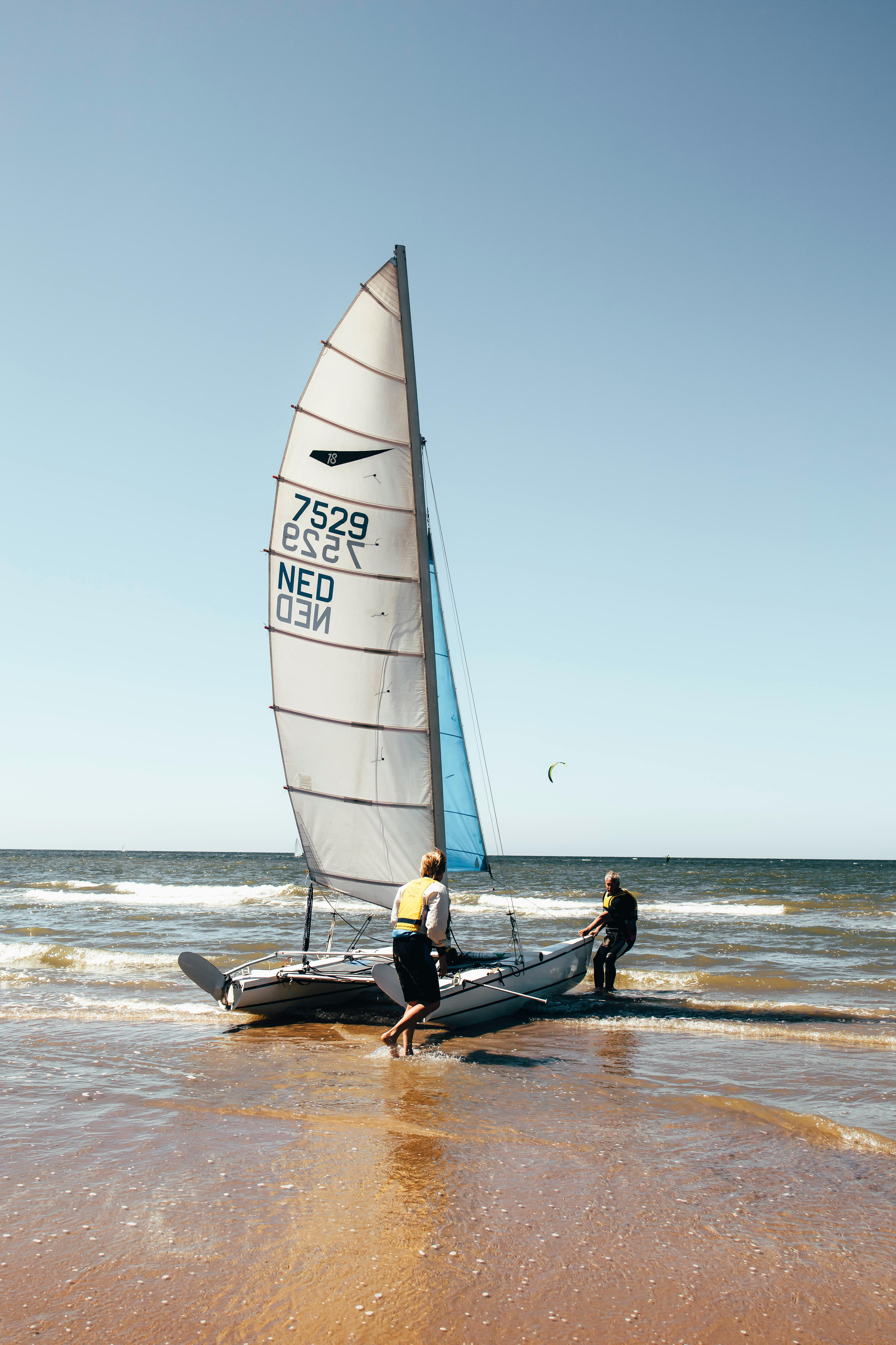 Two Men Launching Sailboat at Beach