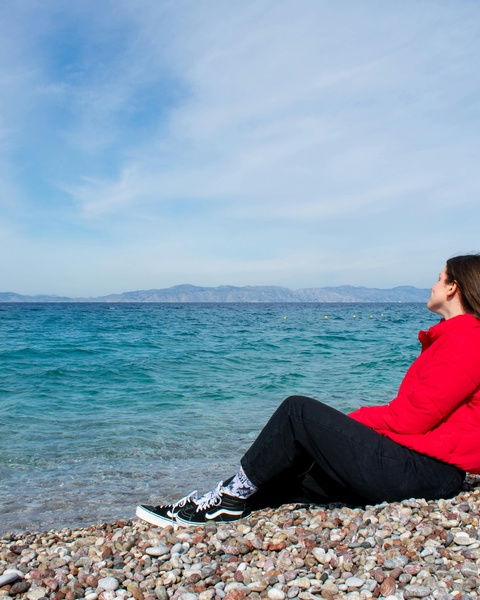 Woman Sitting on Pebble Beach Looking at Sea
