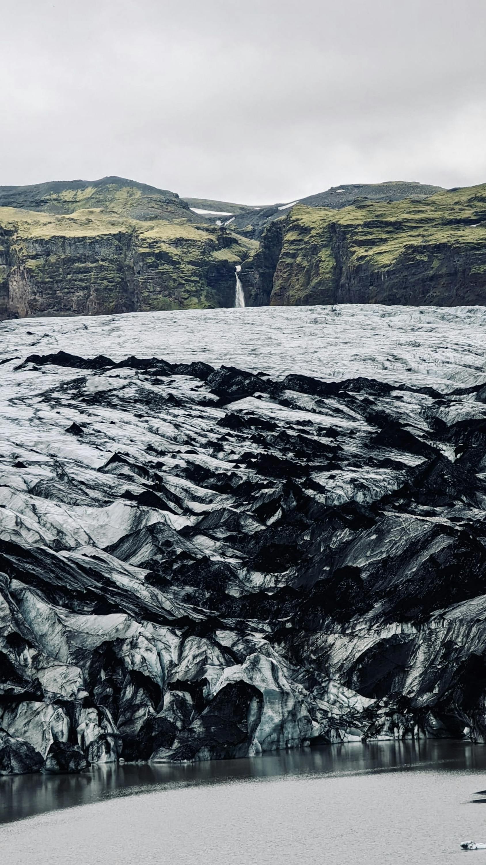Ash-Covered Glacier with Distant Waterfall
