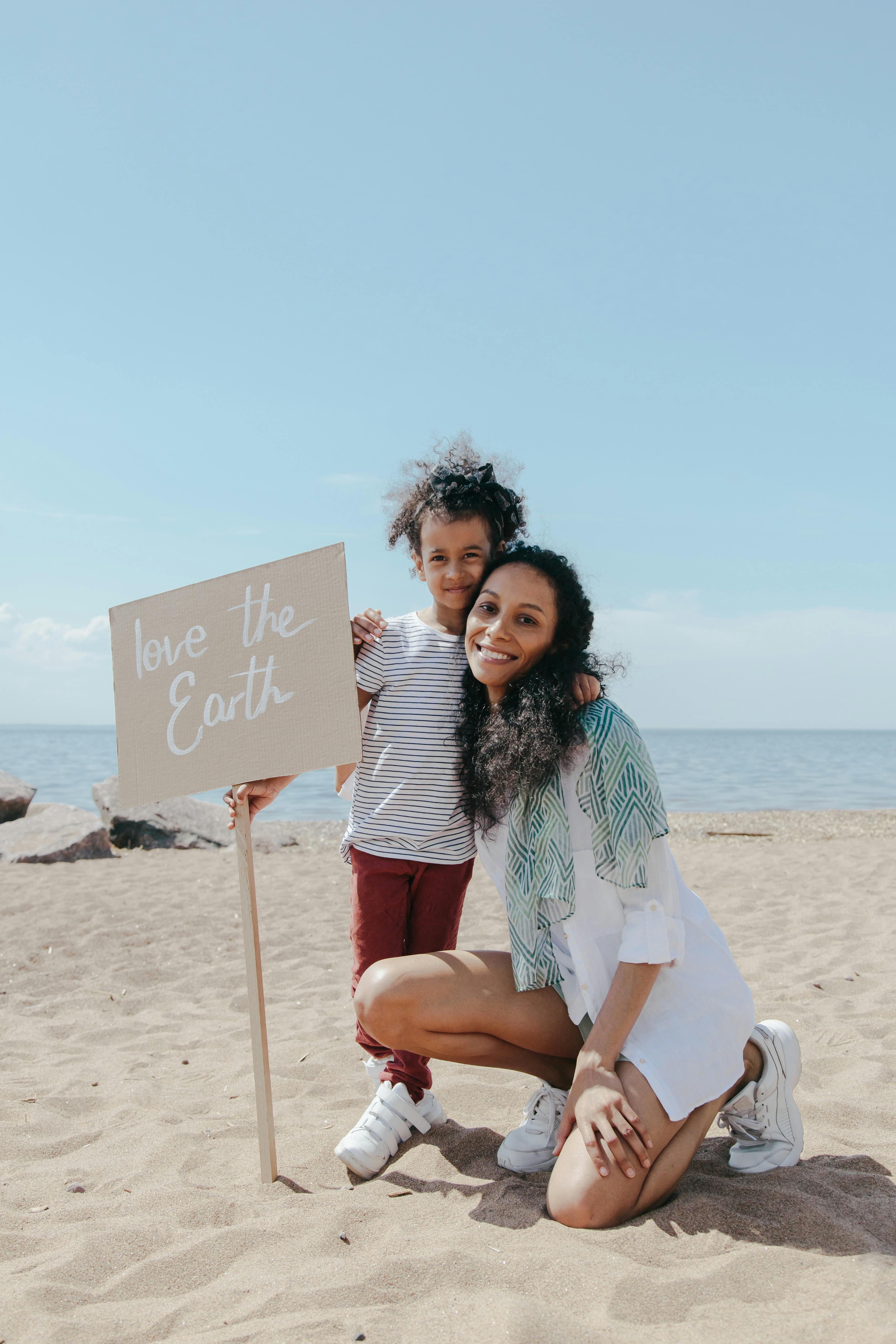 Mother and Child Holding Love the Earth Sign on Beach