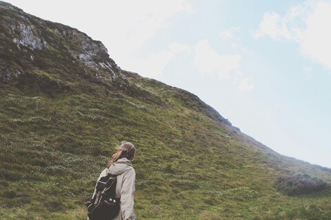 Hiker Ascending Grassy Mountain Slope