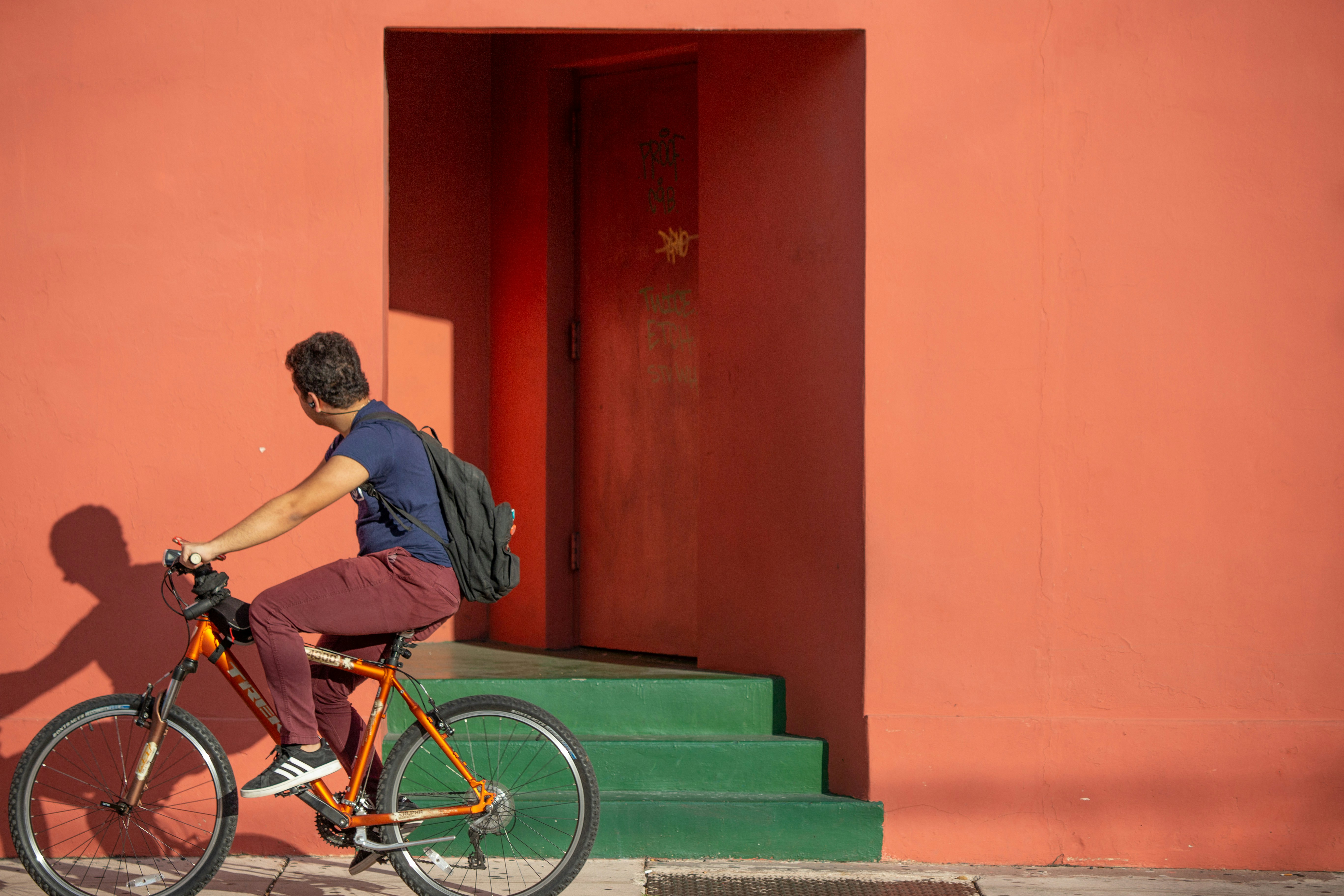 Man cycling past red-orange building wall