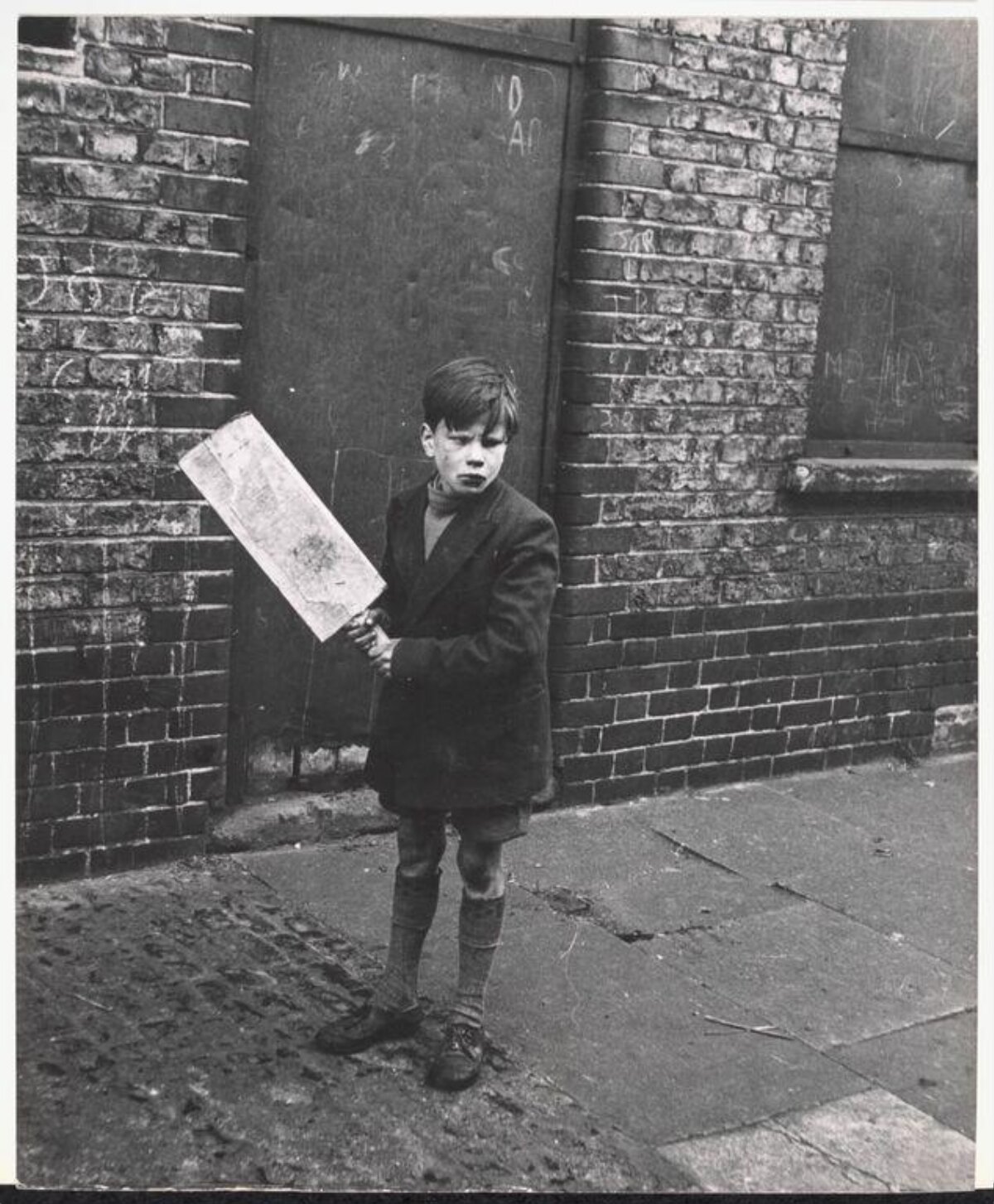 Boy Holding Board by Brick Wall