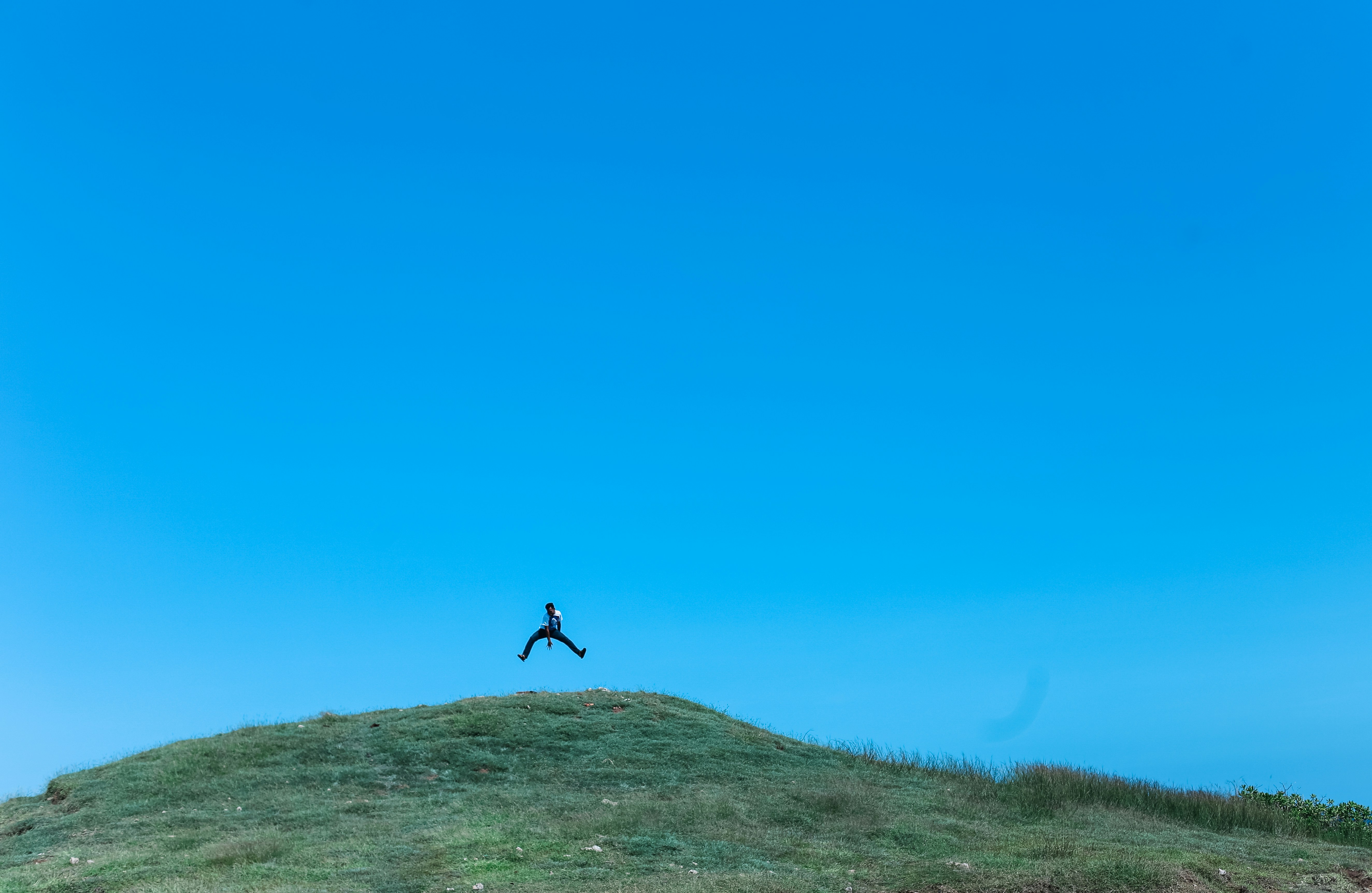 Person Jumping Above Grassy Hilltop