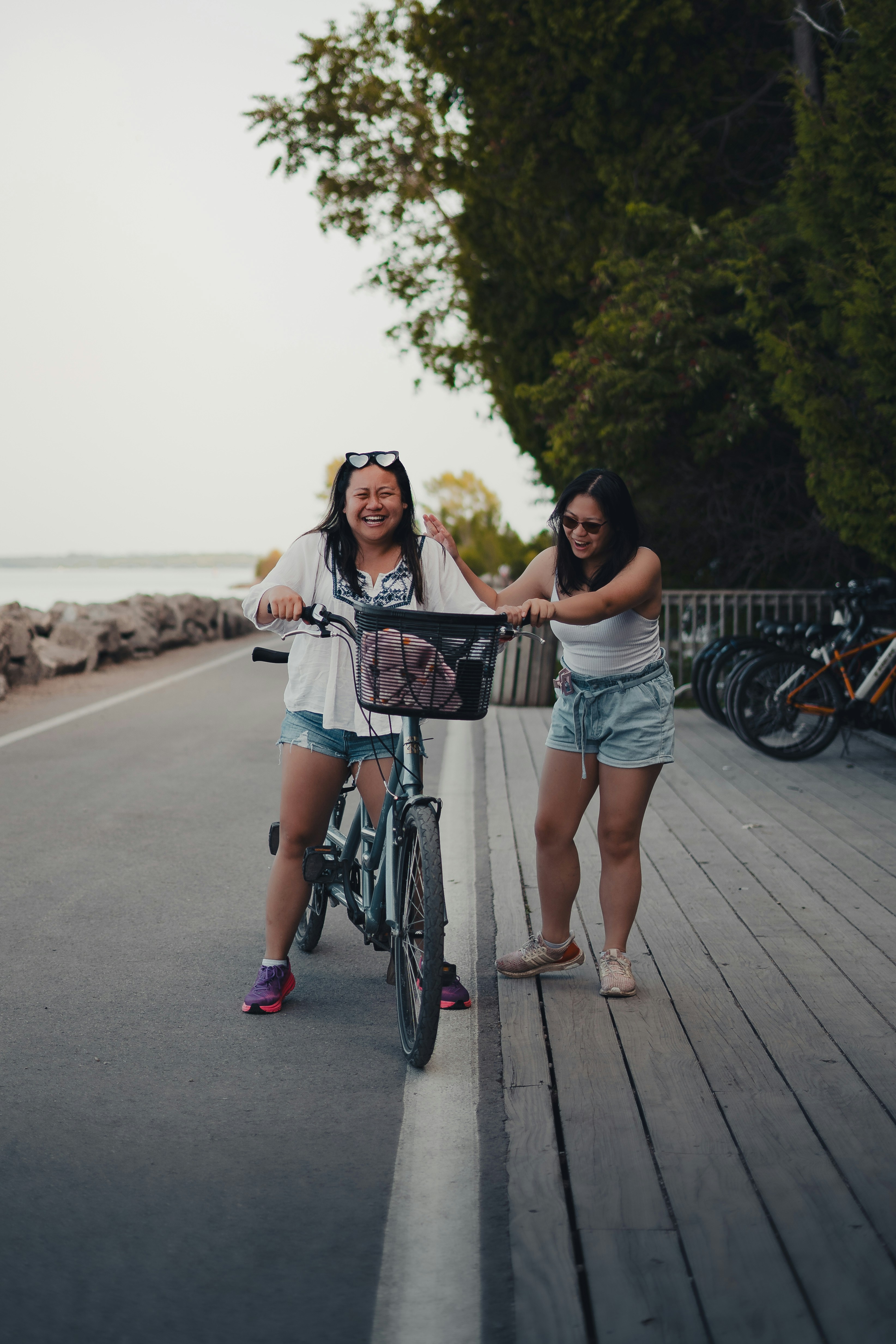 Two Friends Laughing With Bicycle By Waterfront