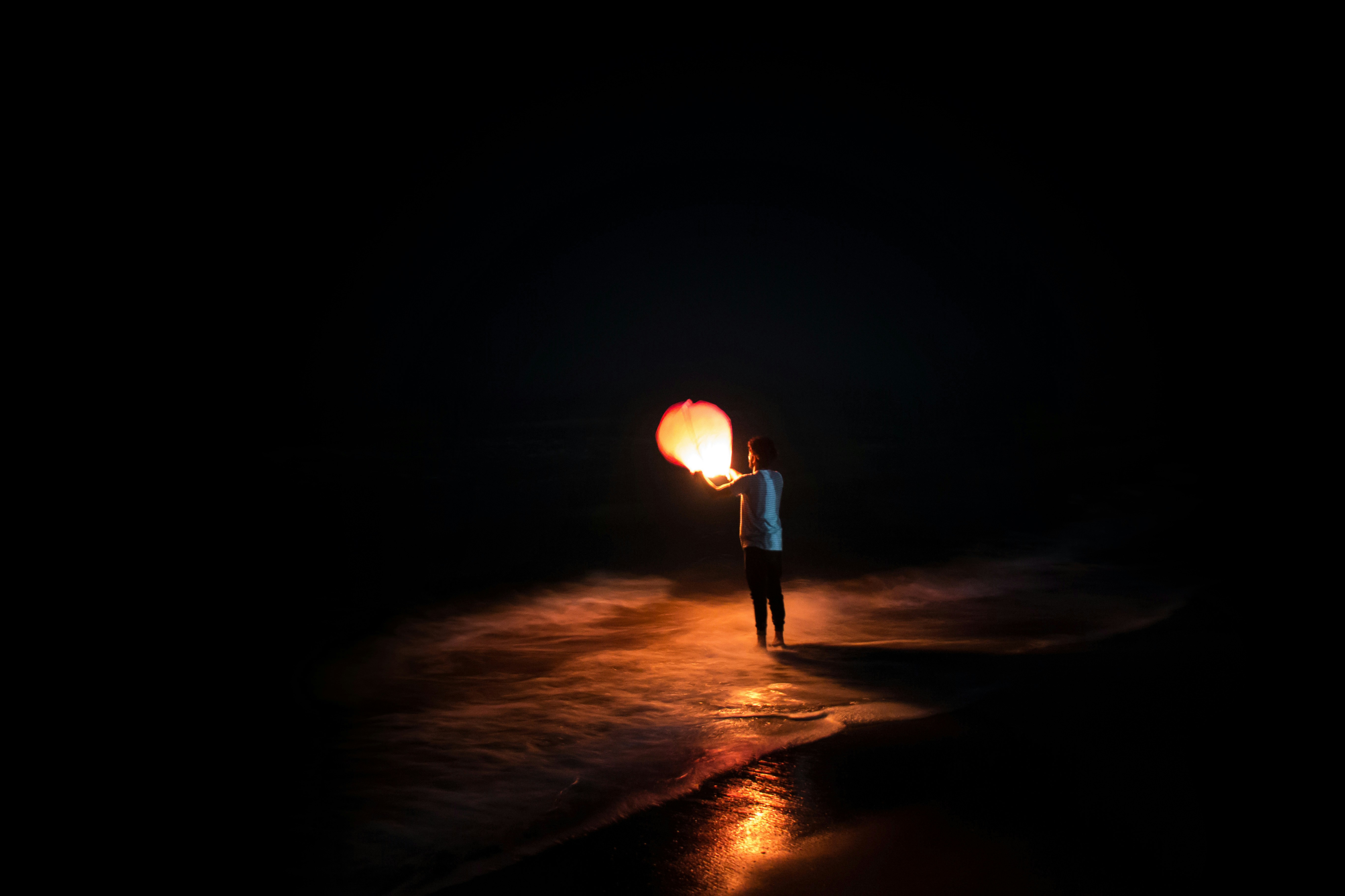 Person Holding Sky Lantern on Night Beach