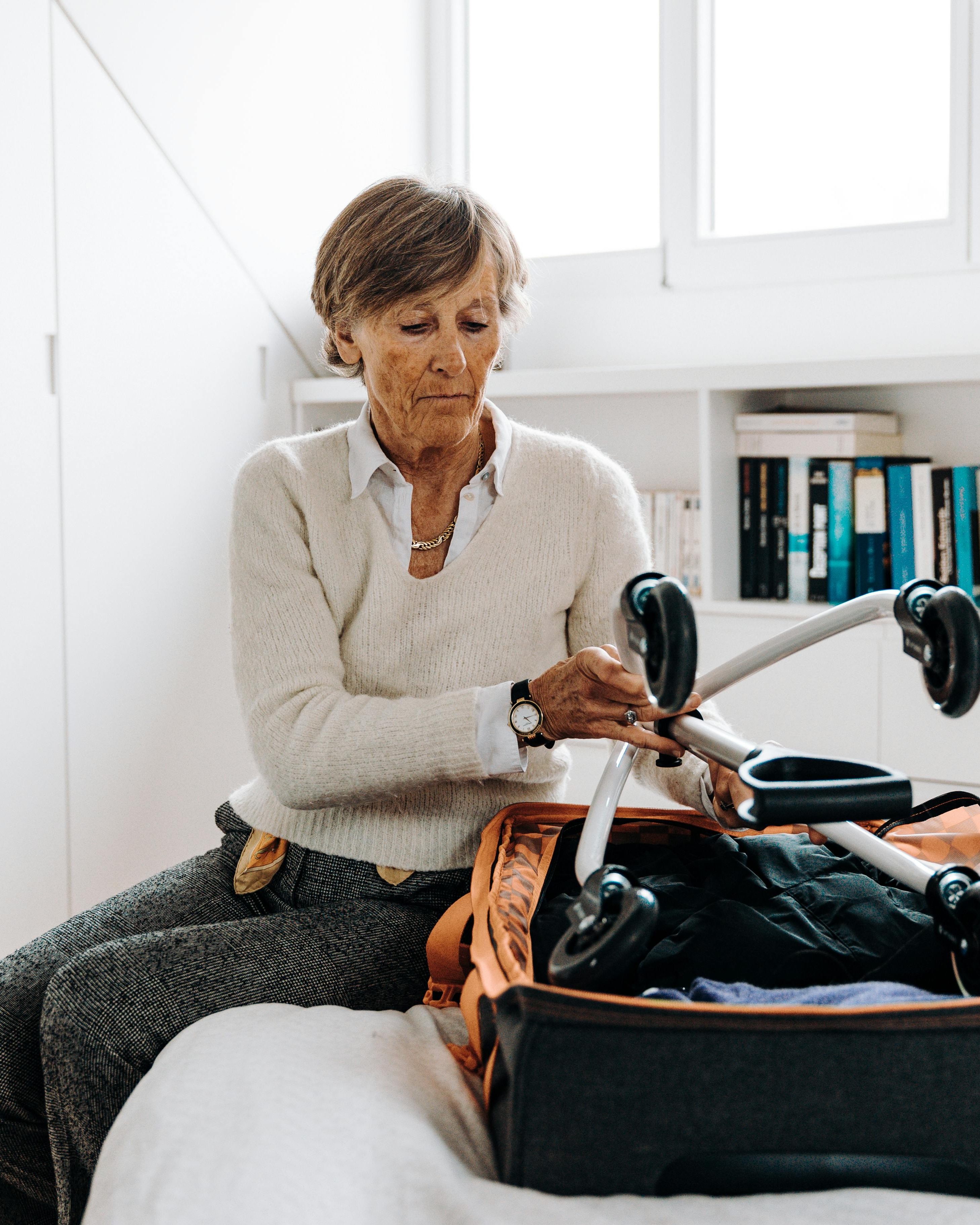 Senior Woman Packing Mobility Walker Into Suitcase