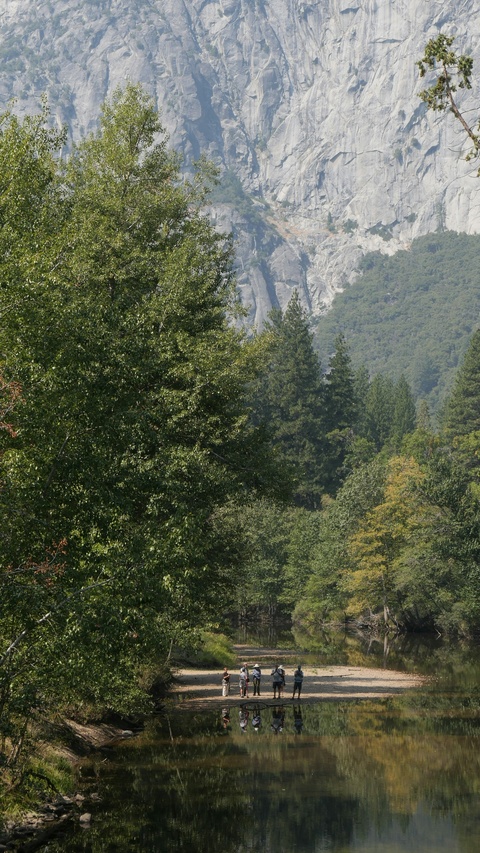 Hikers on Riverbank Beneath Granite Cliffs