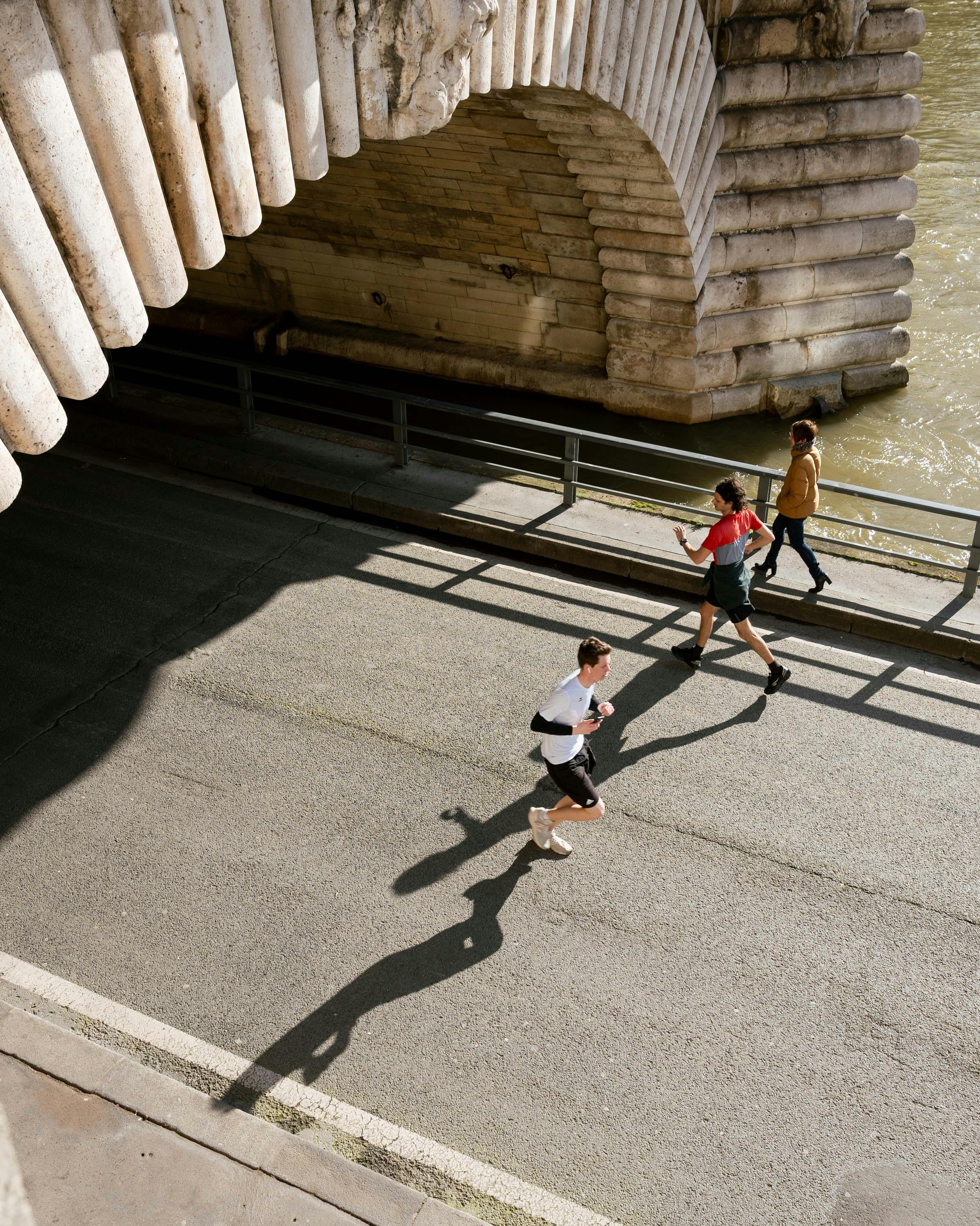 Joggers Running Under Stone Bridge by River