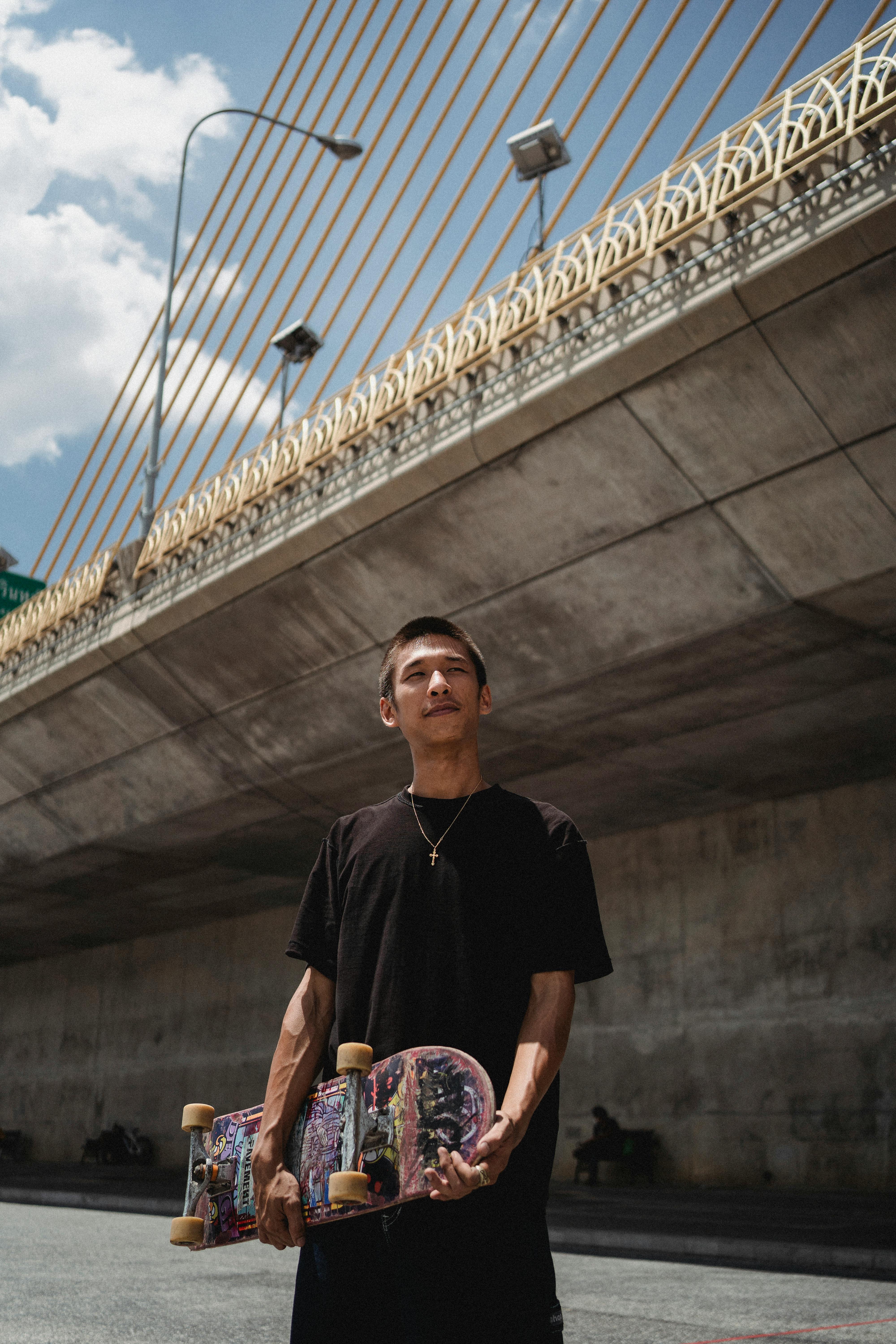 Skateboarder Holding Skateboard Under Bridge