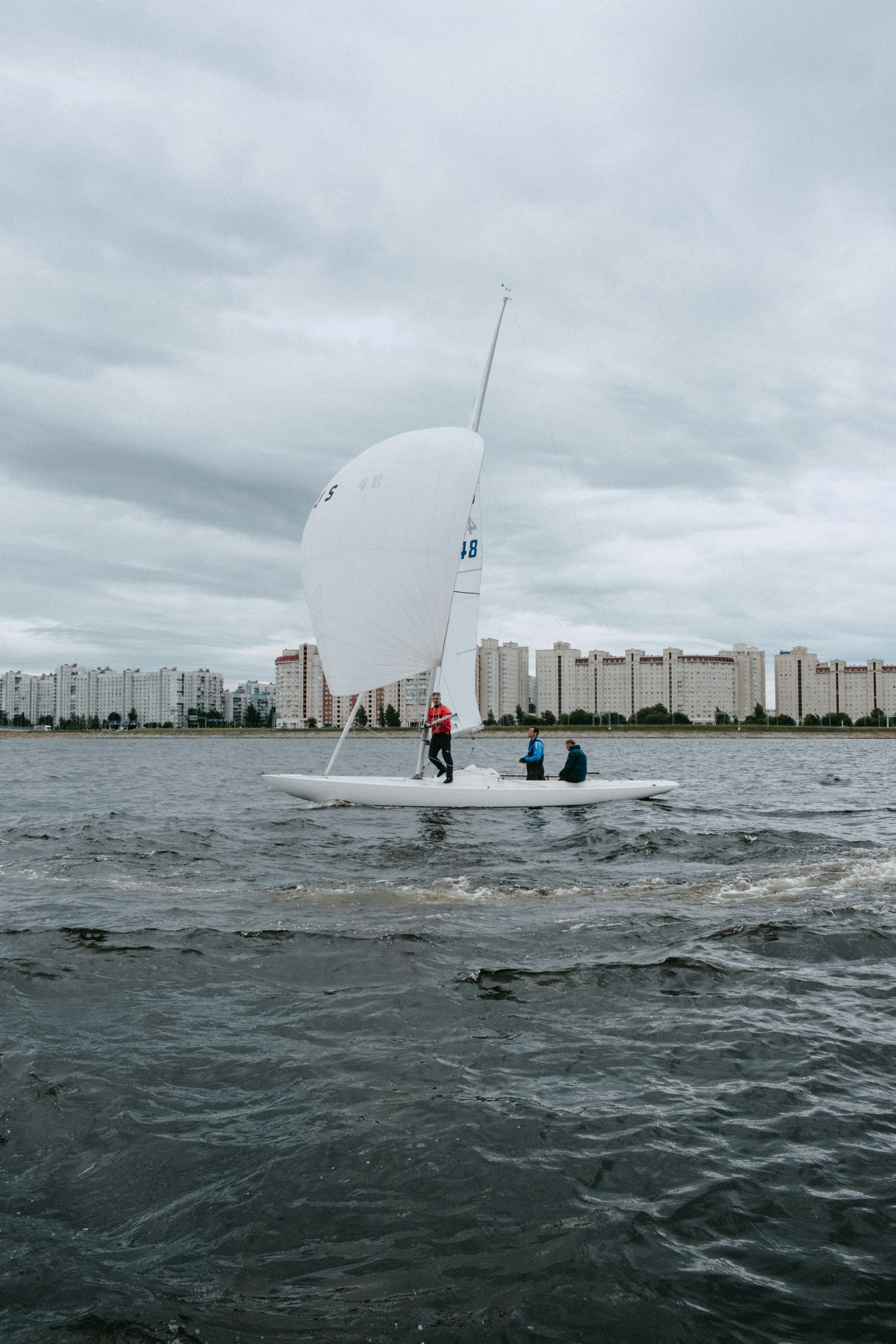 Three People Sailing Near Urban Waterfront
